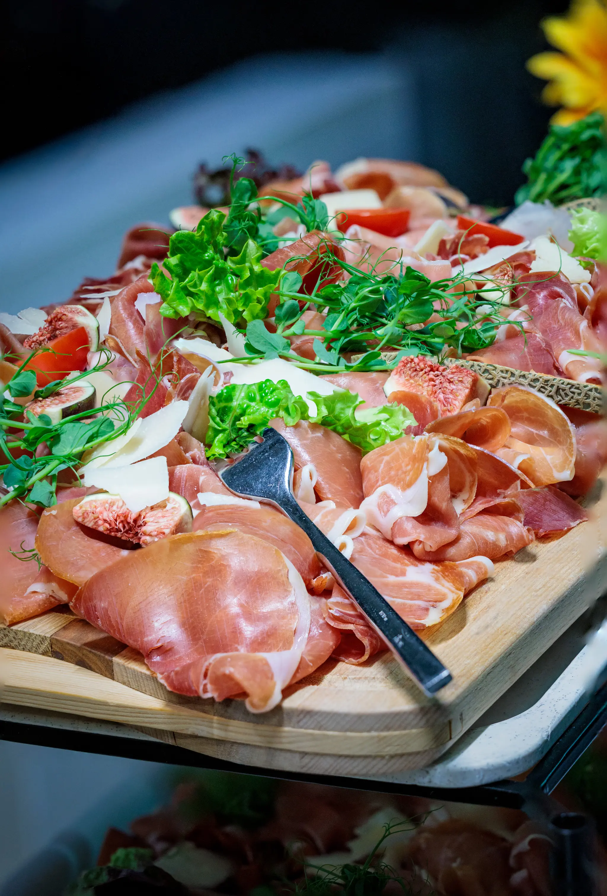 Eine rustikale Aufschnittplatte mit Prosciutto, frischen Feigen und Käsespänen, serviert auf einem Holzbrett im VIP-Bereich bei einem Spiel der Black Wings Linz