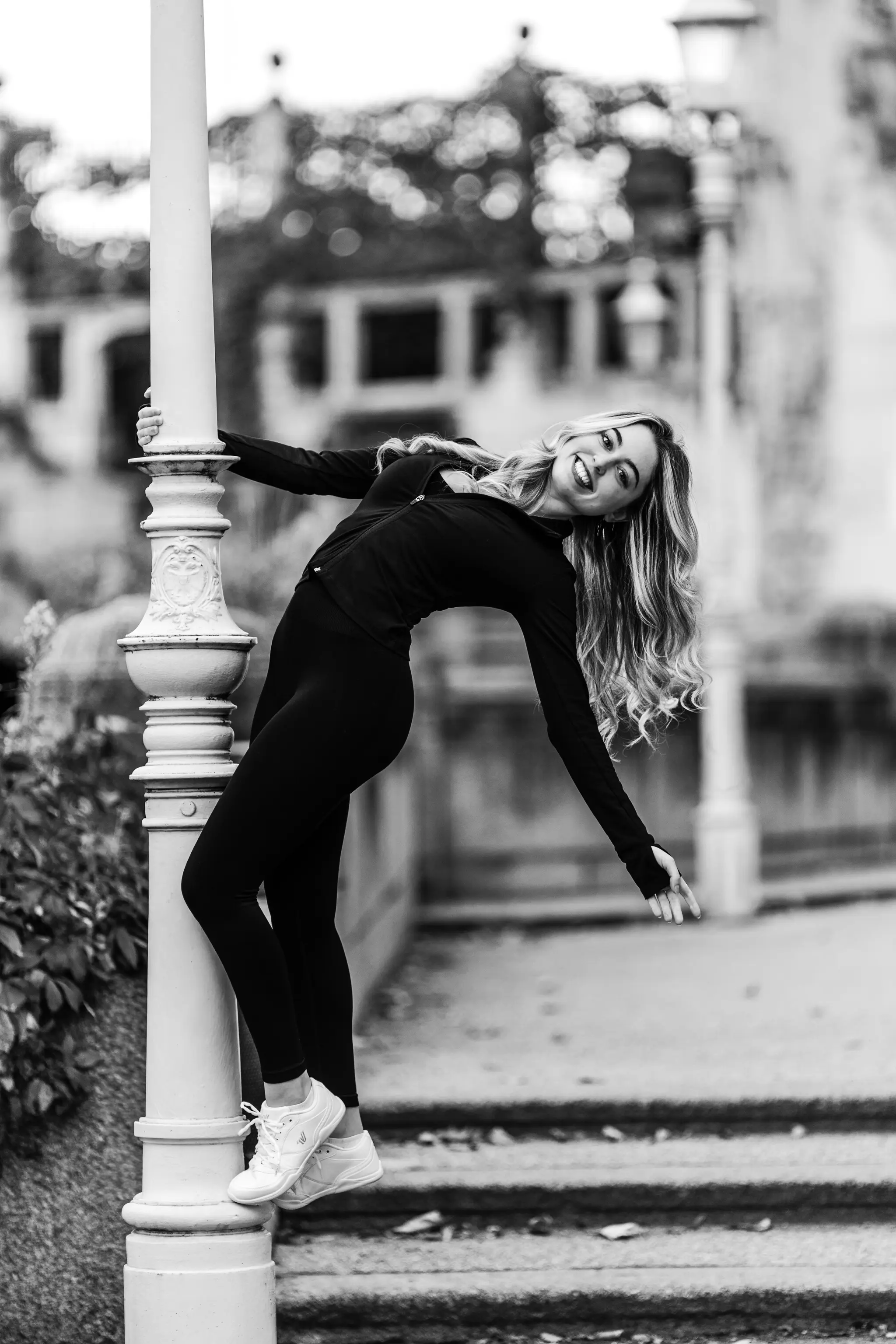 Schwarz-Weiß-Porträt von Model Valentina, die bei einem Fotoshooting im Wiener Stadtpark in sportlicher Kleidung lachend an einer Laterne posiert