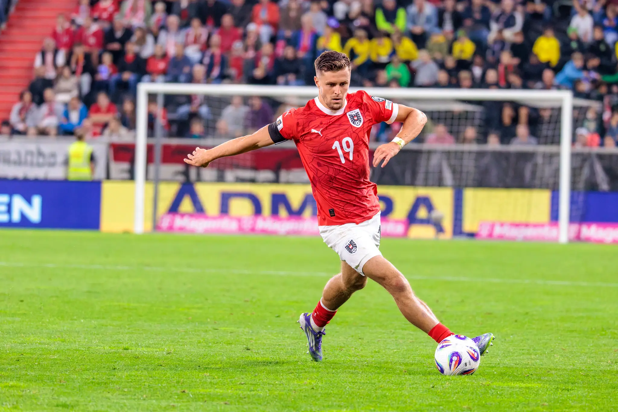 Der österreichische Nationalspieler Christoph Baumgartner kontrolliert den Ball im roten Trikot mit der Nummer 19 während eines Fußballspiels