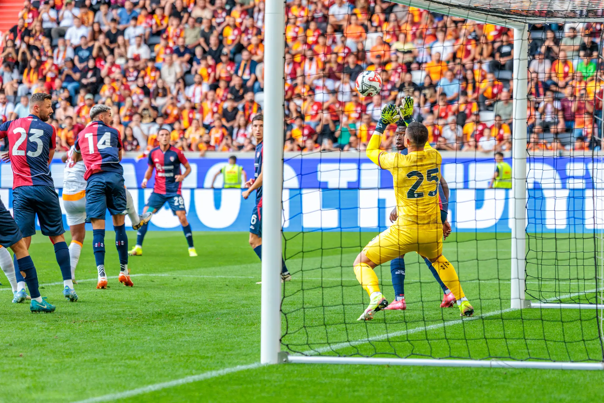 Ein Fußballtorhüter in Gelb pariert einen Schuss während eines Spiels der Nero Summer Series vor einer vollen Tribüne 