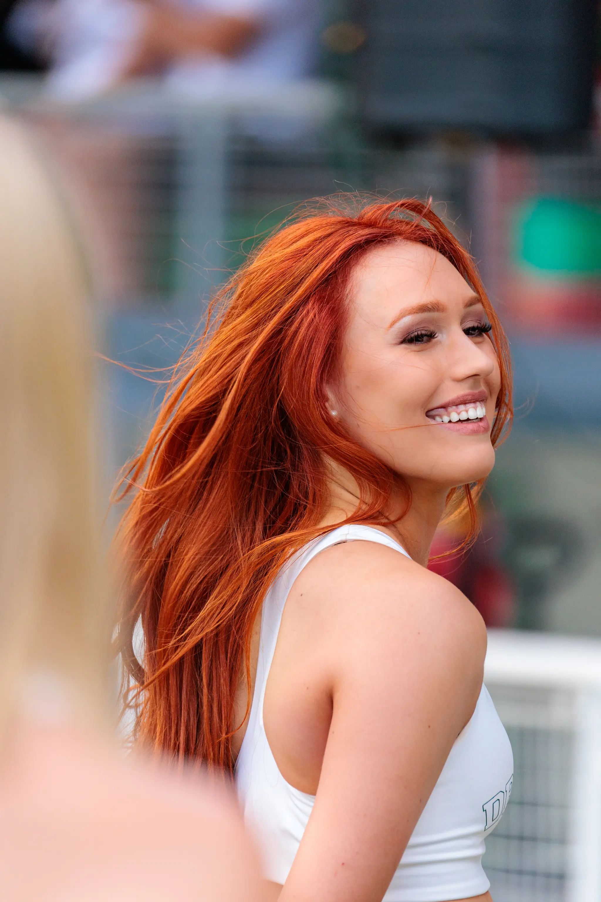 Rothaarige Dragons-Cheerleaderin lächelnd im Seitenprofil, langes rotes Haar, weißes Top bei der Halbzeitshow 2026