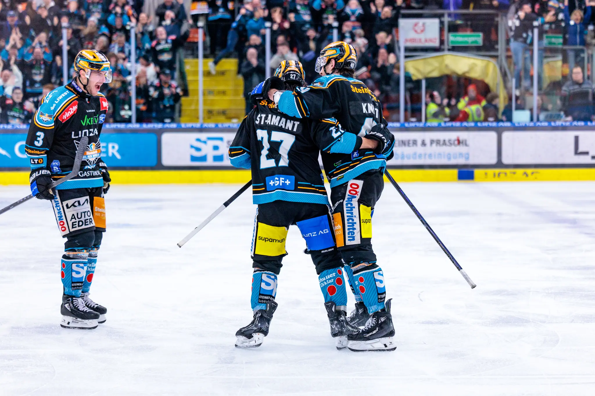 Drei Eishockey-Spieler der Black Wings Linz jubeln gemeinsam auf dem Eis