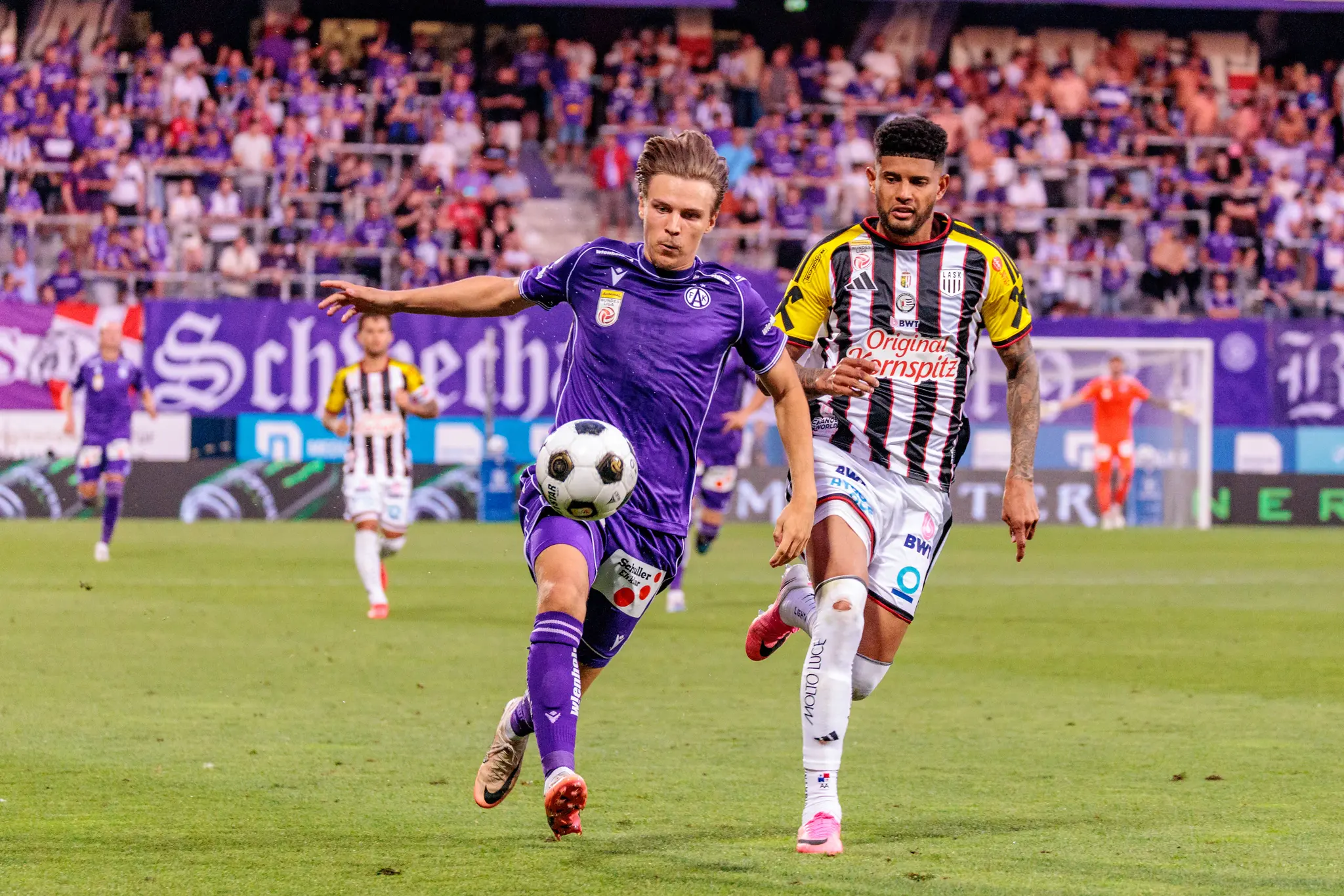 Austria-Spieler nimmt den Ball mit dem Oberschenkel an, ein LASK-Spieler kommt im Zweikampf heran