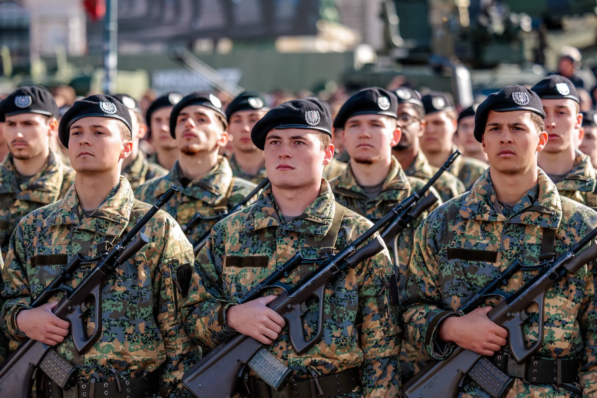 Rekruten in Tarnuniform und schwarzen Baretten sprechen bei der Angelobung die Worte „Ich gelobe“ und halten ihre Sturmgewehre vor der Brust.