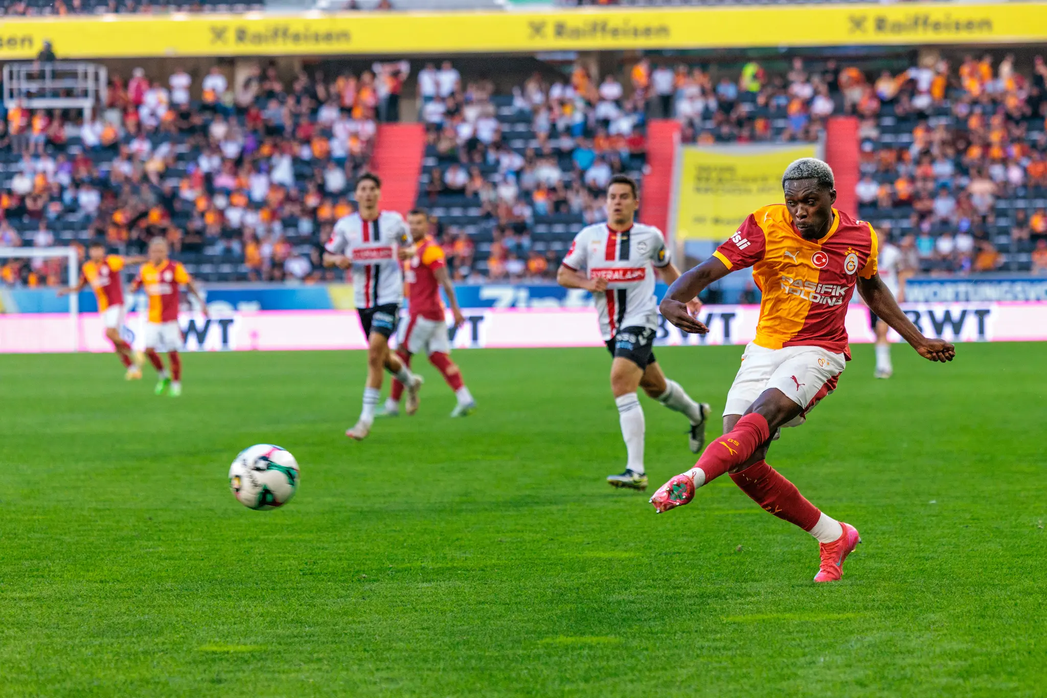 Ein Fußballspieler von Galatasaray Istanbul tritt den Ball während eines Spiels in der Raiffeisen Arena vor einer gefüllten Tribüne 