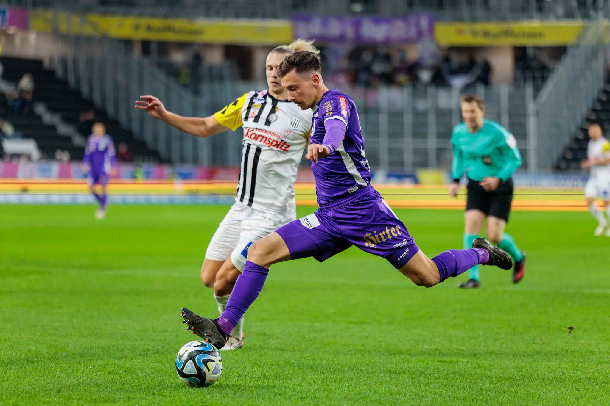 Ein Fußballspieler im lila Trikot tritt den Ball während eines Bundesligaspiels in der Raiffeisen Arena