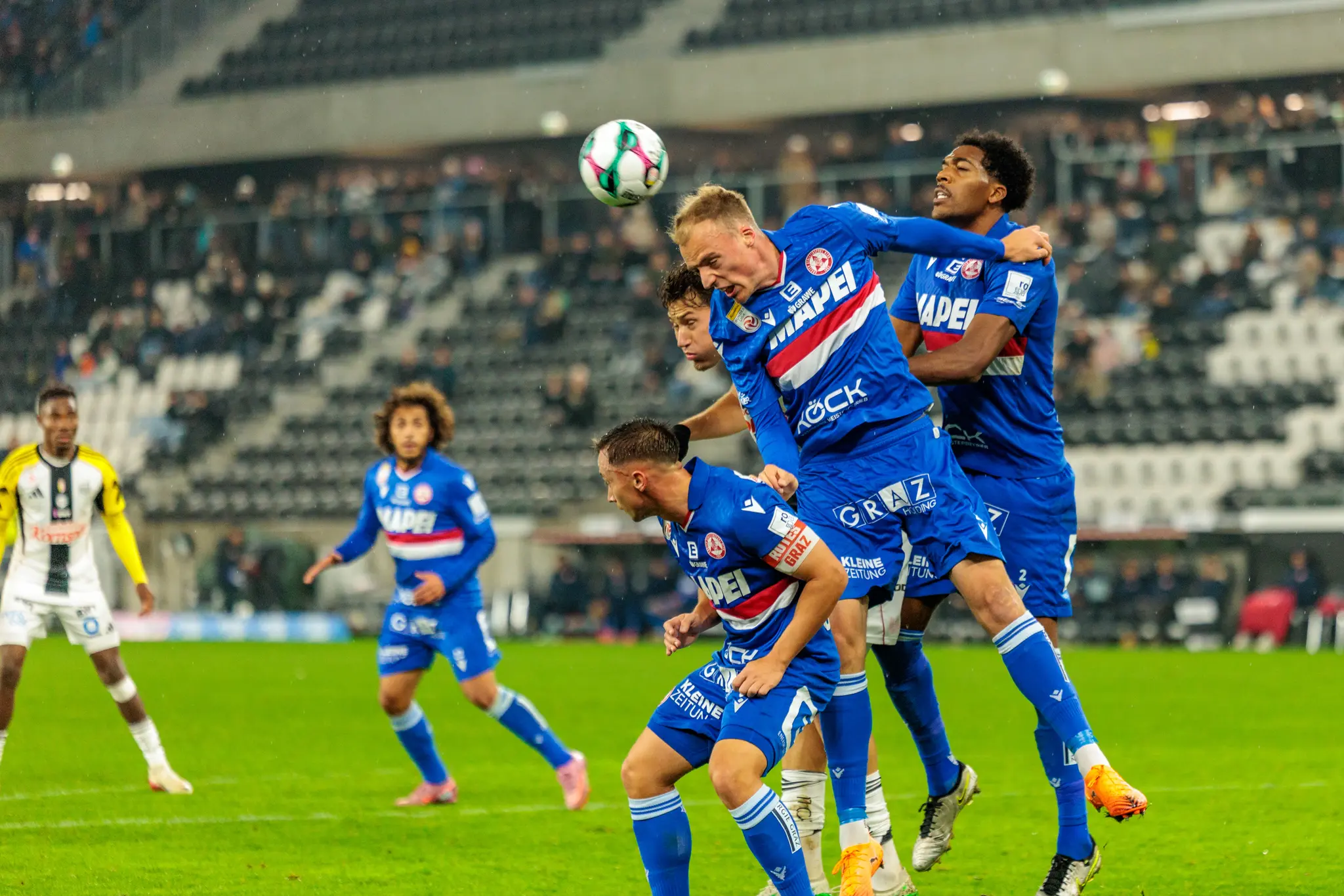 Intensives Kopfballduell eines GAK-Spielers in blauer Dress, der im Spiel gegen den LASK entschlossen zum Ball springt