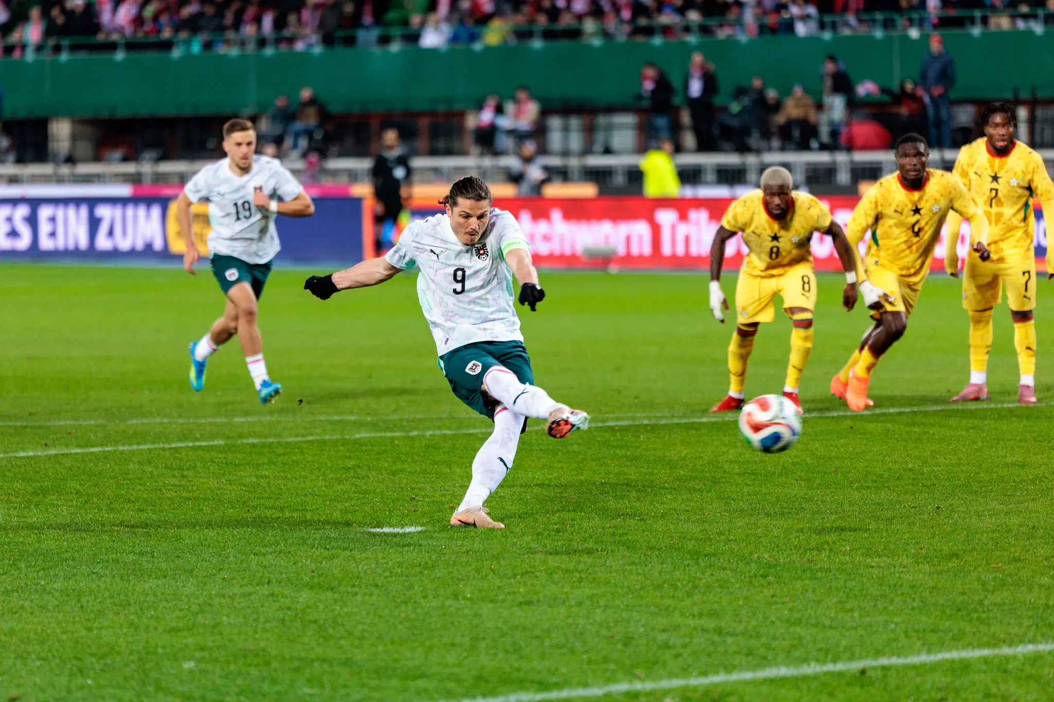 Ein österreichischer Fußballspieler mit der Nummer 9 schießt während eines Länderspiels gegen ghanaische Gegenspieler einen Elfmeter auf das Tor