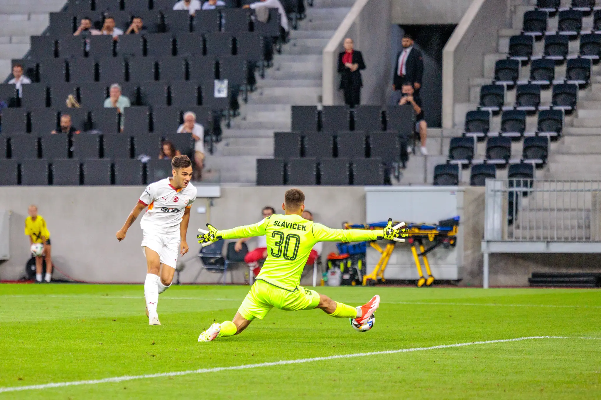 Fußballer von Galatasaray im weißen Trikot vor Torhüter Slavíček in leuchtend grünem Dress, der im Stadion nach dem Ball taucht 