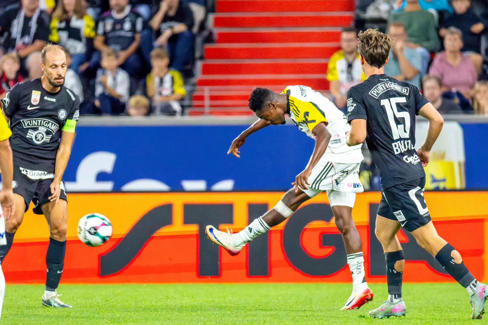 Ein Spieler des LASK schießt den Fußball, umgeben von zwei Spielern des SK Sturm Graz