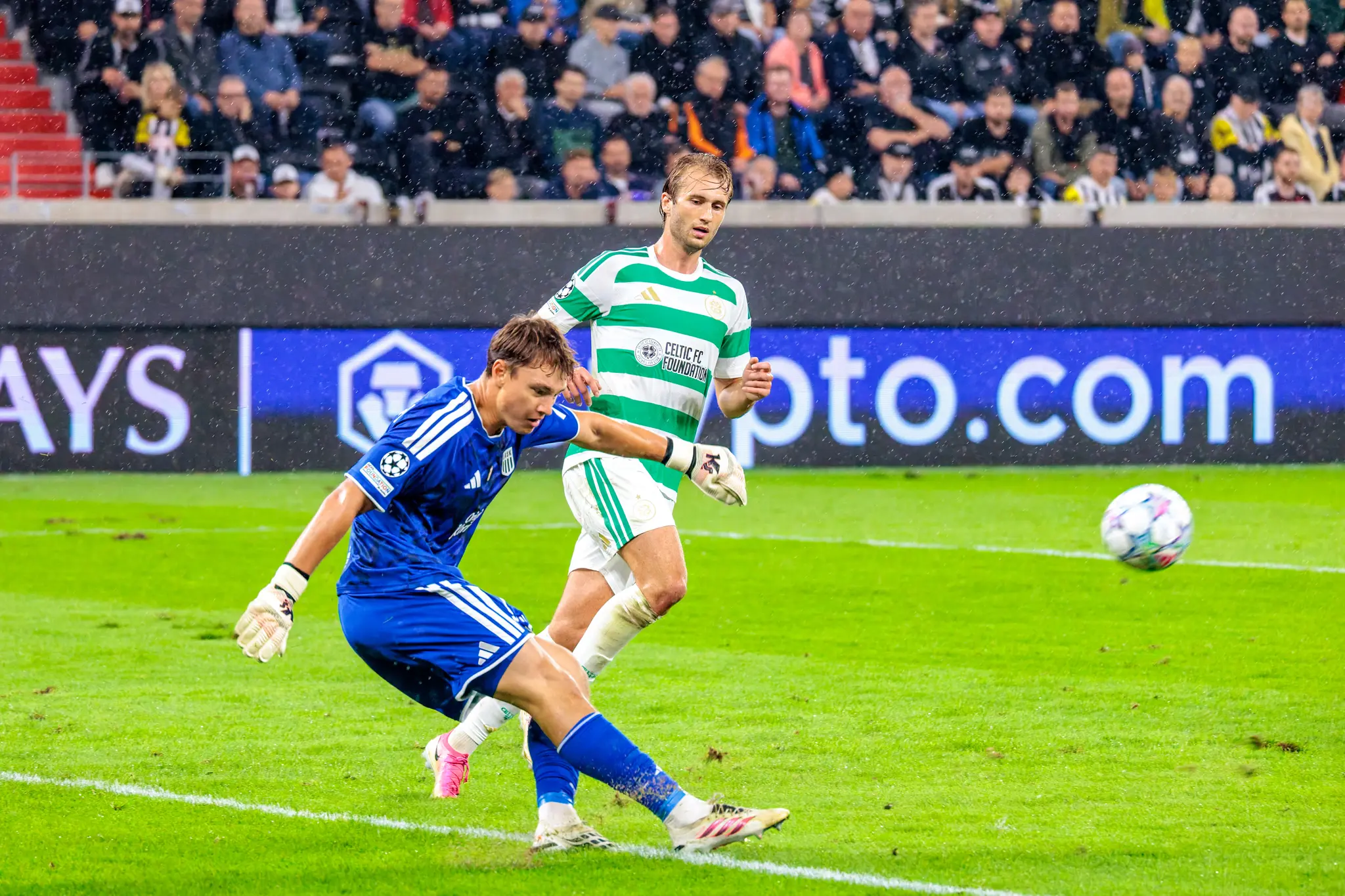 Kurz vor der Pause kein Zaudern: LASK-Keeper Jungwirth klaert unter Druck, ein Celtic-Angreifer sitzt ihm im nassen Ruecken.