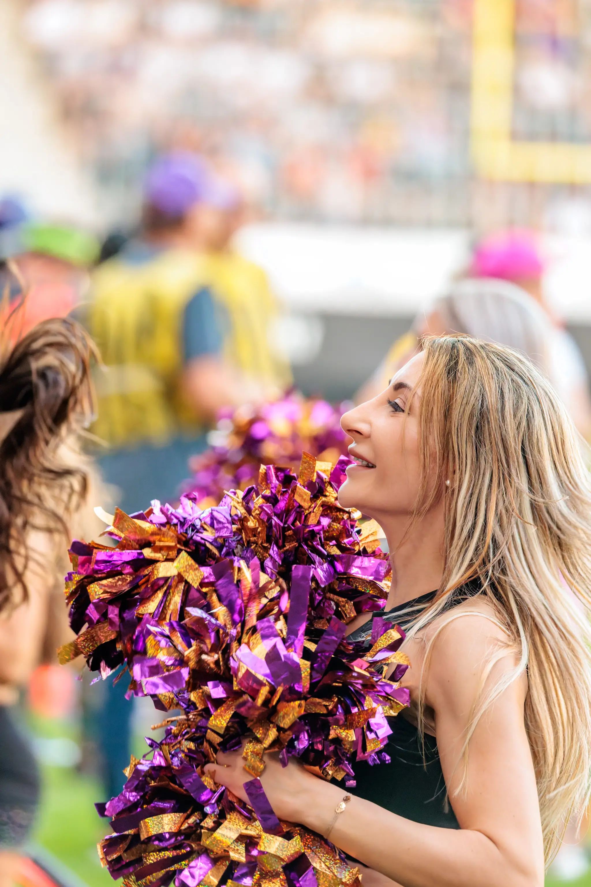 Im Profil hält eine blonde Tänzerin des Vienna Vikings Cheer Squads ihre lila-goldenen Pompons dicht vor dem Körper.