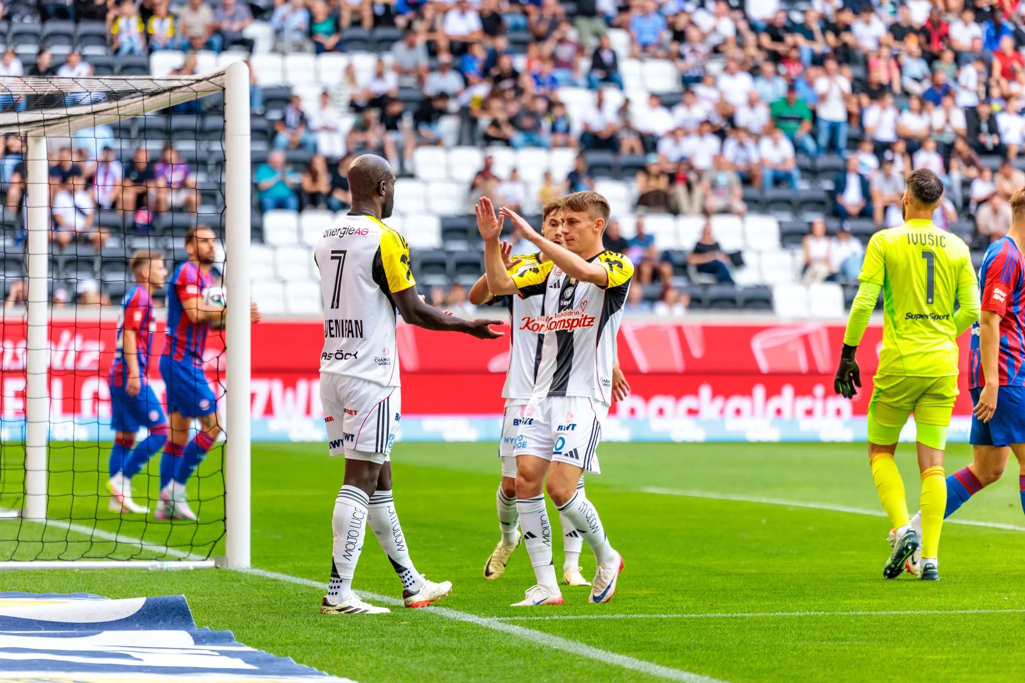 LASK Fußballspieler im schwarz-weißen Trikot feiern einen Torerfolg während eines Spiels der Nero Summer Series in der Raiffeisen Arena vor einer Tribüne voller Zuschauer 