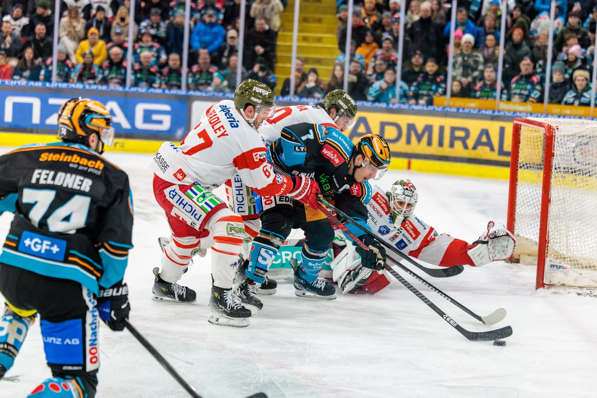 Dynamische Eishockey-Spielszene mit mehreren Spielern, Puck und Torwart vor dem Tor 