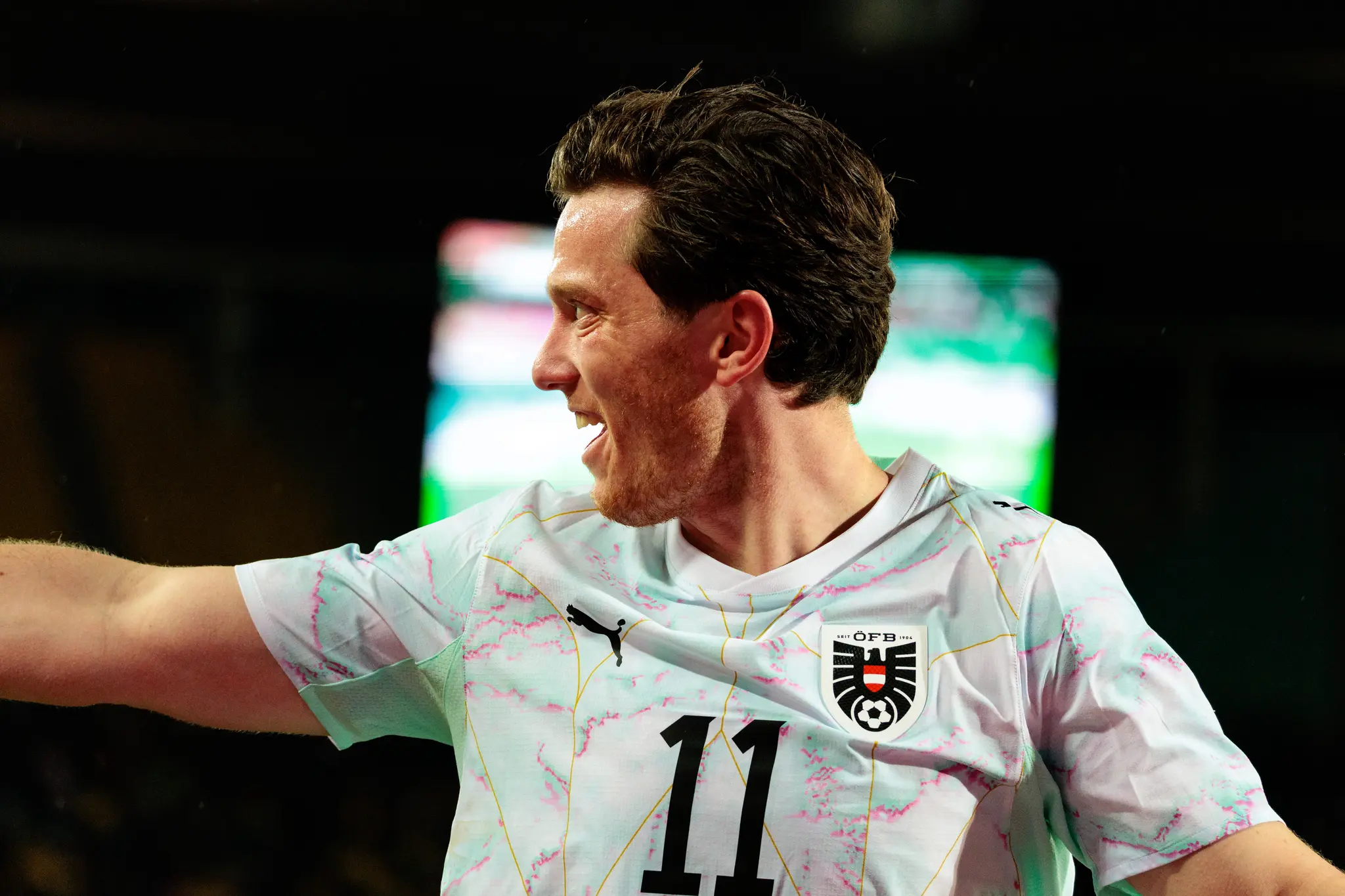 Ein österreichischer Fußballspieler im Trikot mit der Nummer 11 jubelt strahlend mit offenem Mund und Blick zur Seite
