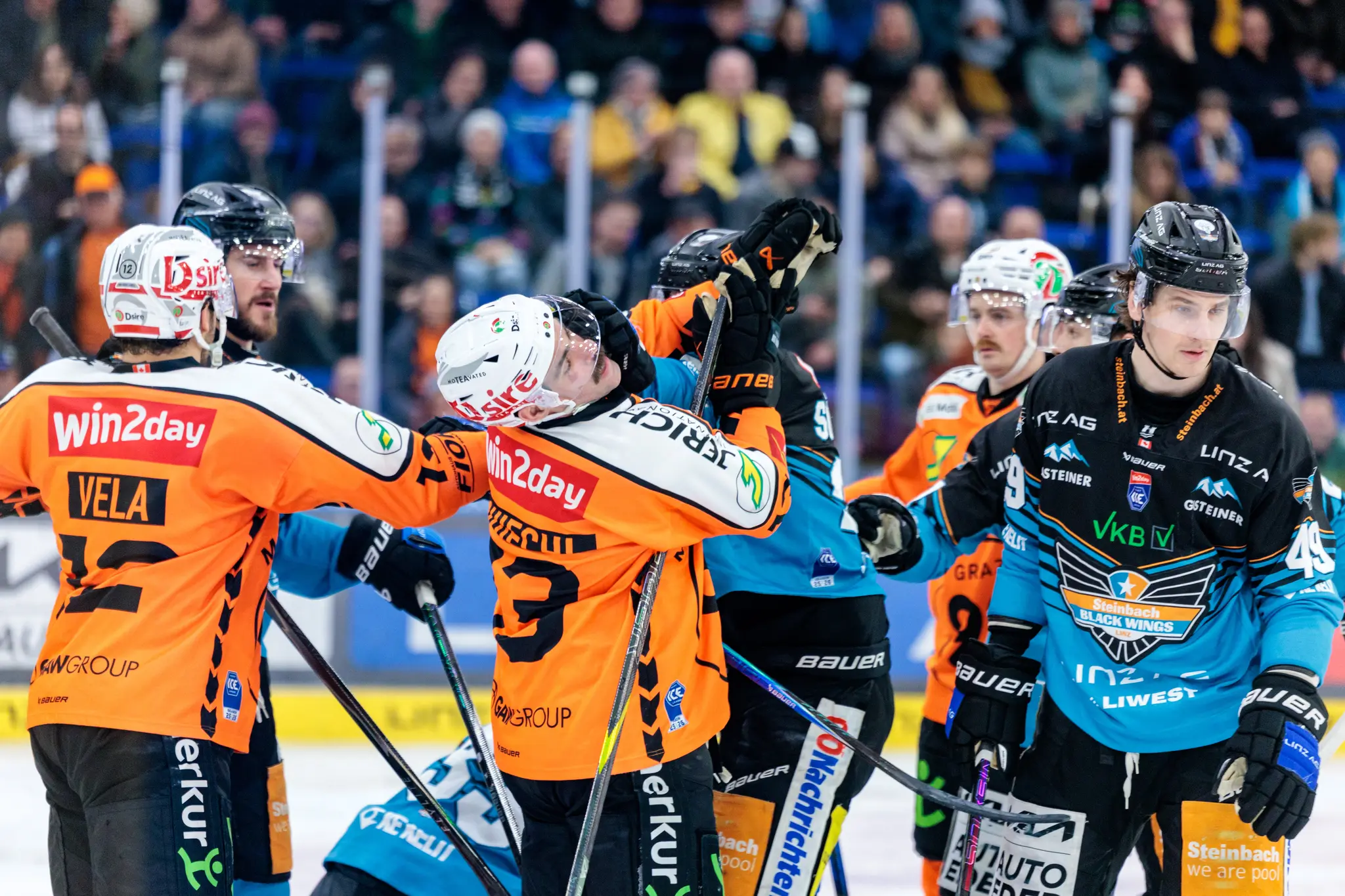 Eishockeyspieler in orangefarbenen und blau-schwarzen Trikots sind in ein hitziges Gerangel auf dem Eis verwickelt