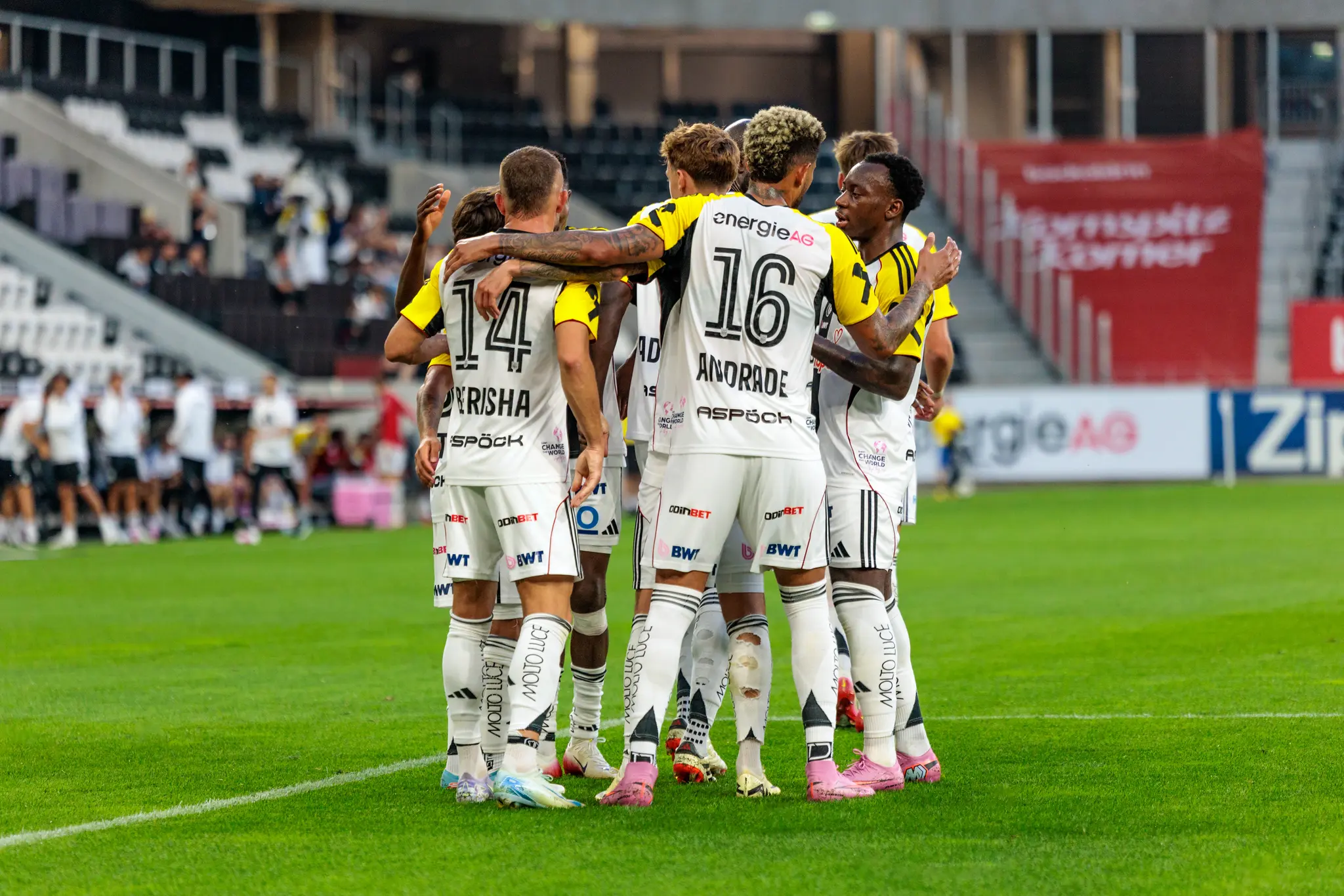 Mehrere LASK Fußballspieler in hellen Trikots bilden während eines Nero Summer Series Vorbereitungsspiels einen engen Kreis auf dem Spielfeld 