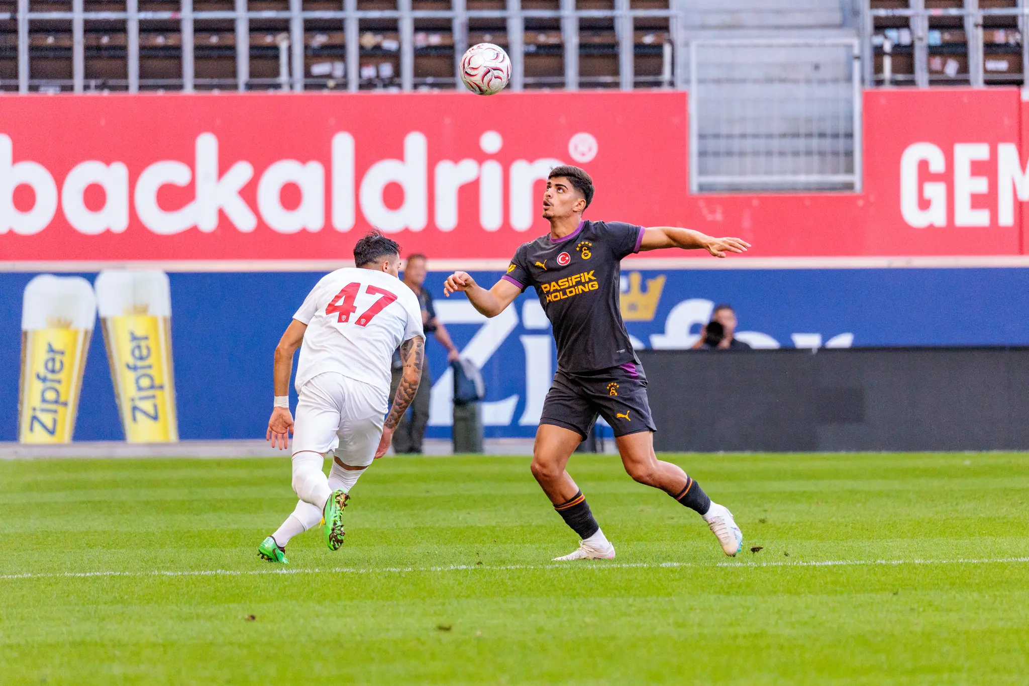 Luftzweikampf zwischen Galatasaray-Spieler im dunklen Trikot und Monza-Spieler Nummer 47, beide Arme und Blick zum Ball in der Luft.