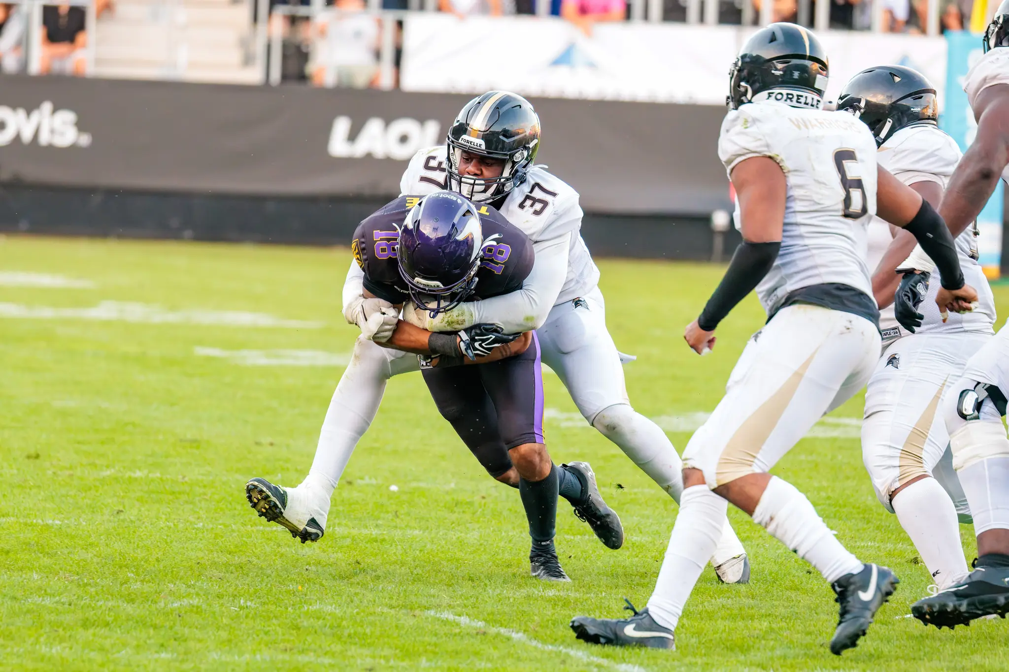 Noah Touré (18) der Vienna Vikings wird nach dem Fang von einem London-Verteidiger (37) zu Fall gebracht – ein weiterer Warrior (6) beobachtet das Tackle im zweiten Viertel.