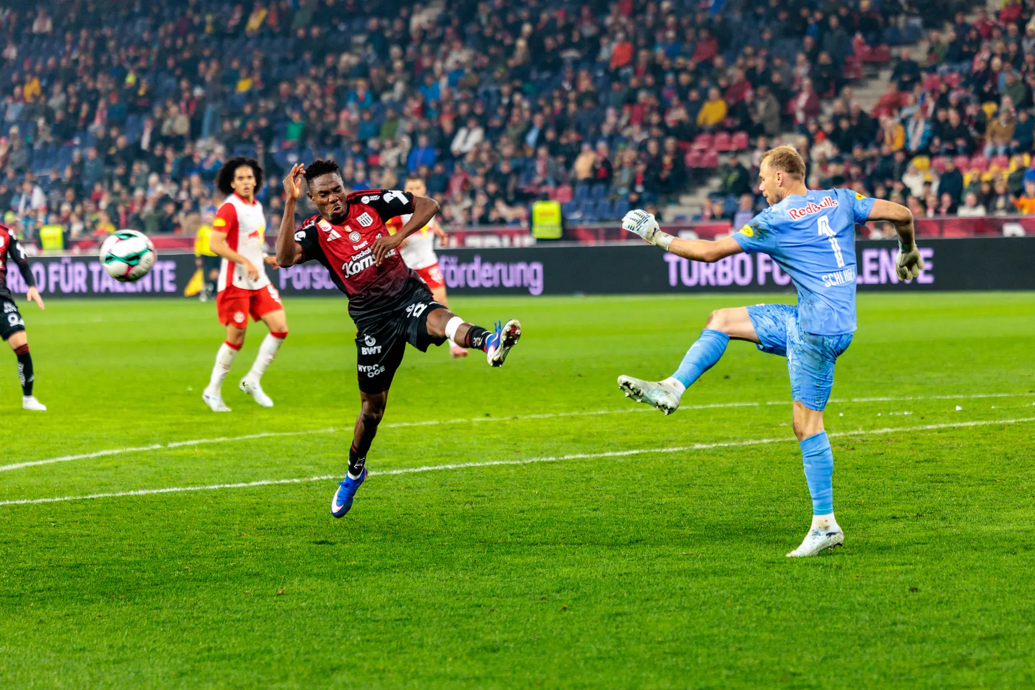 Der Torwart von Red Bull Salzburg klärt einen Ball vor einem sich mit einem Sprung nähernden LASK-Spieler