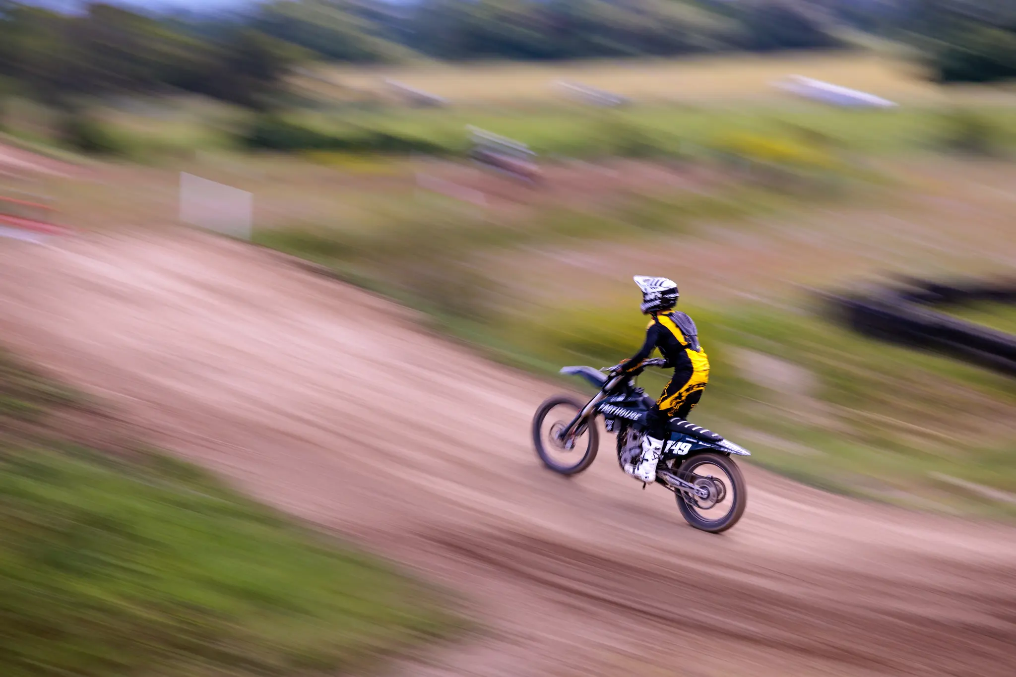Motocross-Fahrer in gelb-schwarzem Rennanzug in voller Fahrt auf seinem Crossbike auf einer Dirtbike-Strecke 