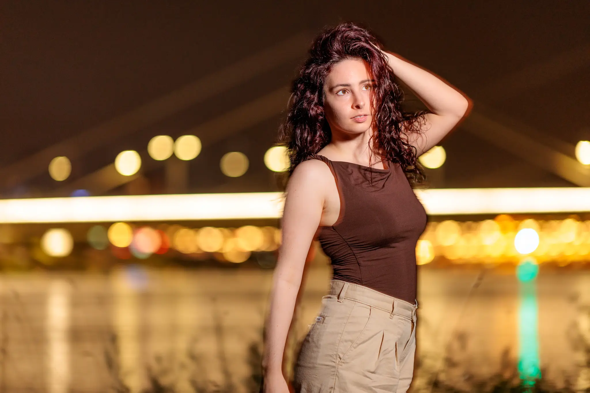 Ein atmosphärisches Nachtporträt von Nicole mit lockigem Haar, die vor einem unscharfen Hintergrund aus goldenen Stadtlichtern in Linz posiert