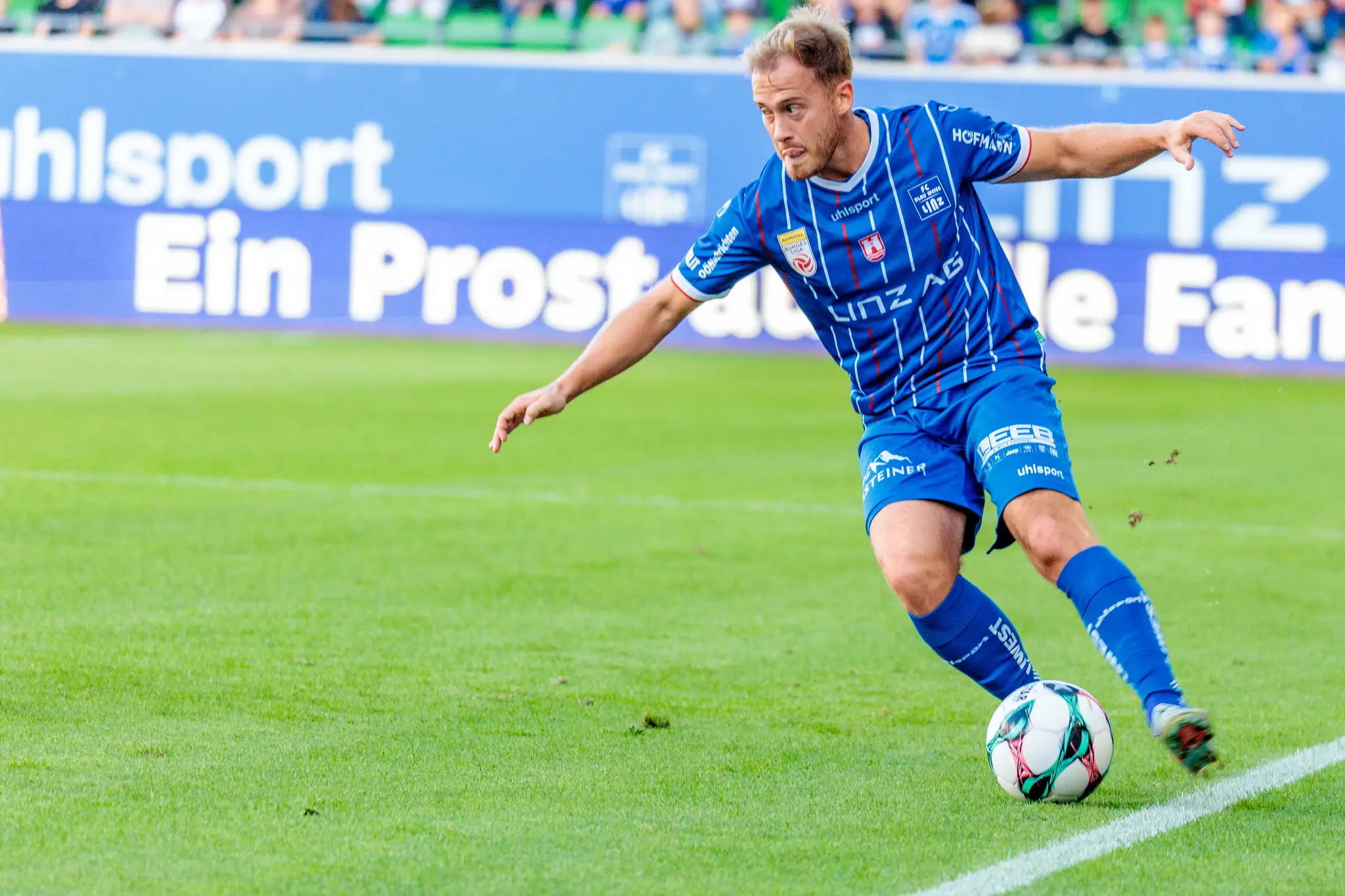 Dominik Reiter im blau-weißen Trikot von Blau-Weiß Linz dribbelt den Fußball mit konzentriertem Blick während eines Spiels