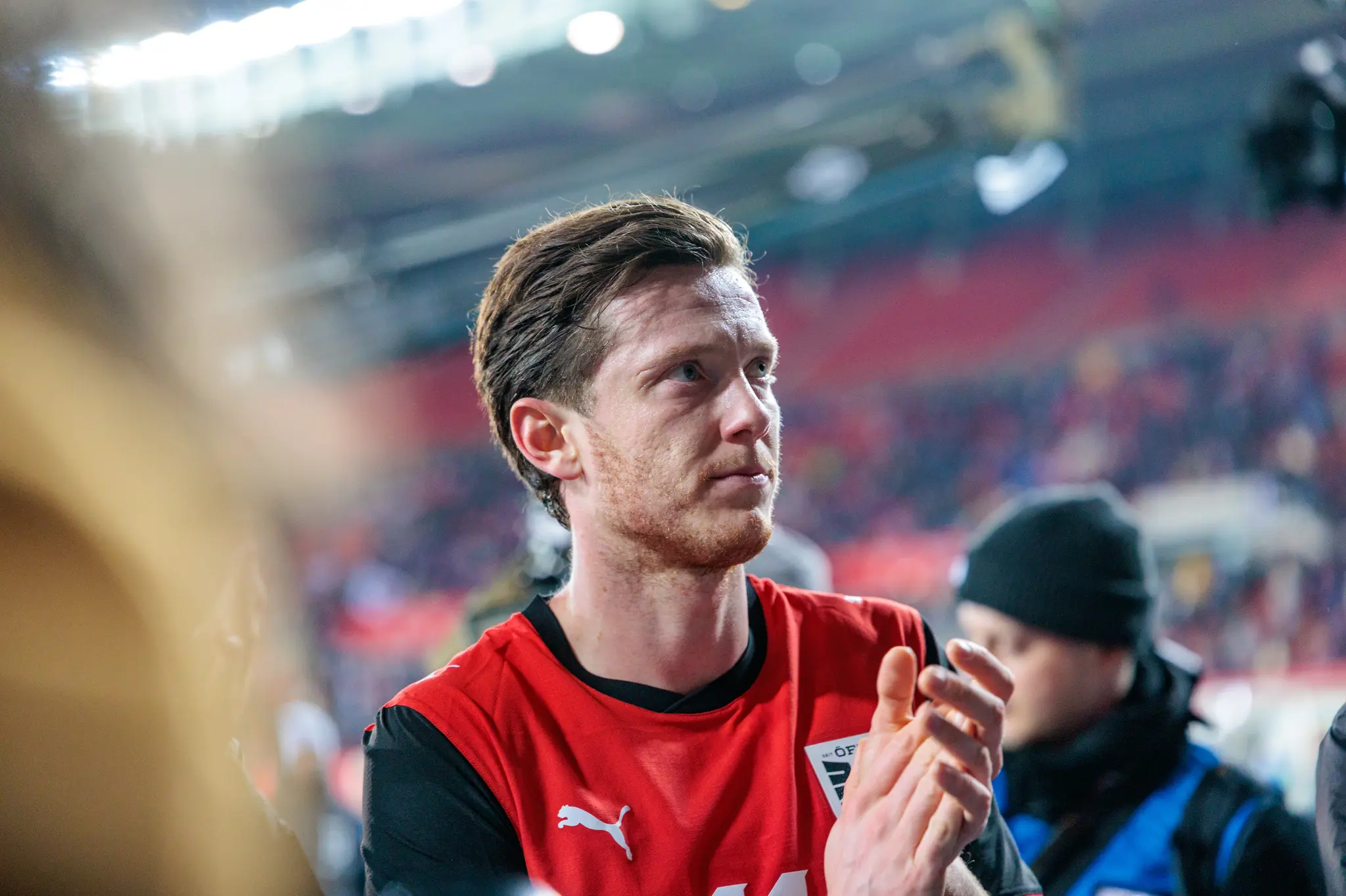 Ein österreichischer Fußballnationalspieler in einem rot-schwarzen Trikot applaudiert seinen Fans im Stadion