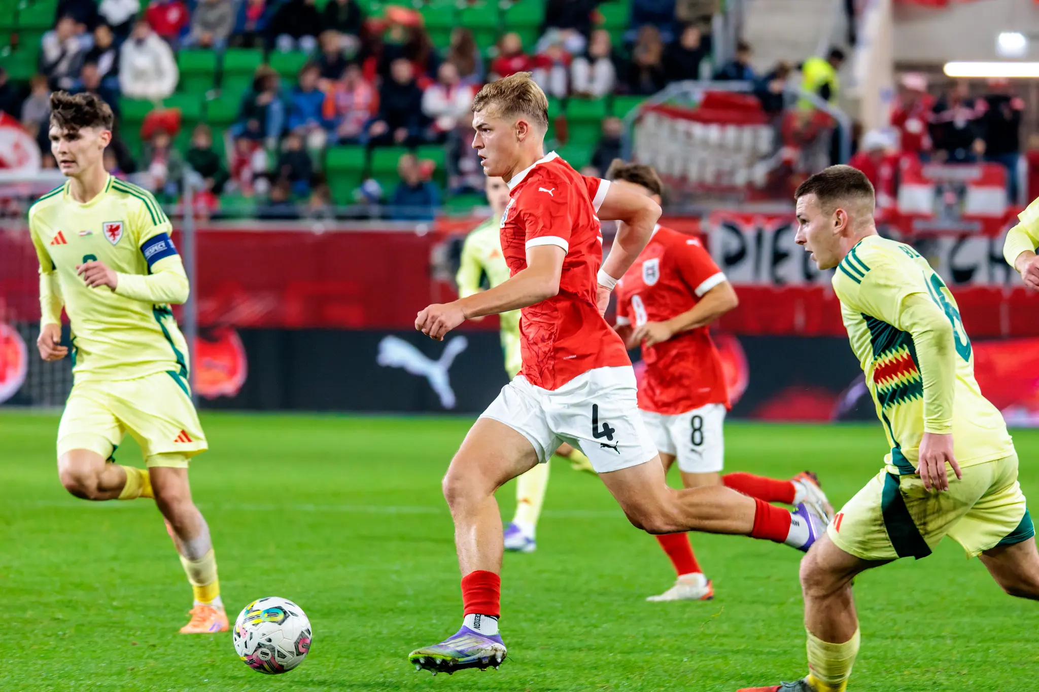 Der österreichische U21-Nationalspieler David Piczka sprintet im roten Trikot mit dem Ball am Fuß, während er von einem walisischen Gegenspieler verfolgt wird