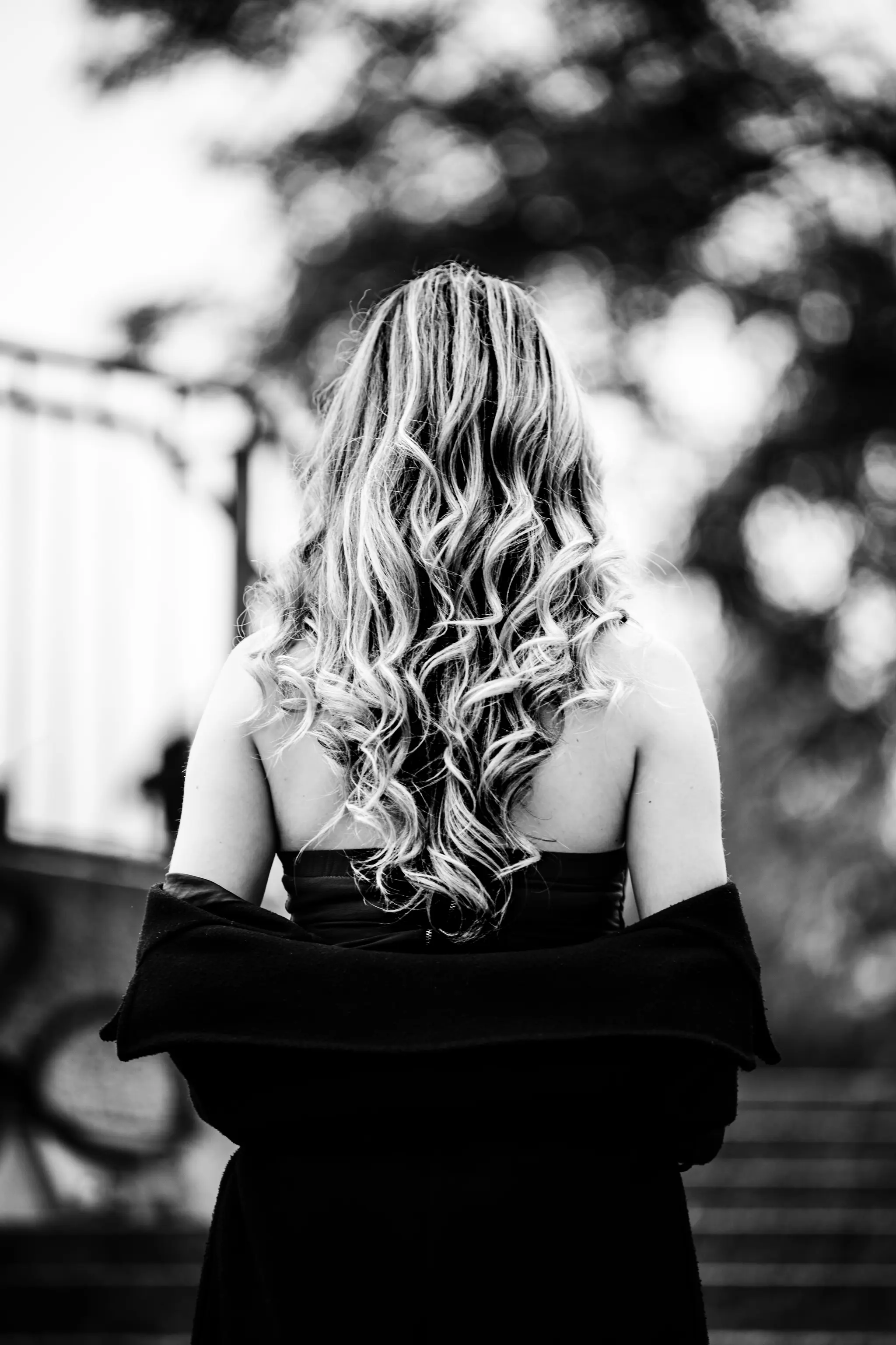 Schwarz-Weiß-Porträt von Model Valentina von hinten, deren lange, blonde Lockenpracht über ihre entblößten Schultern fällt