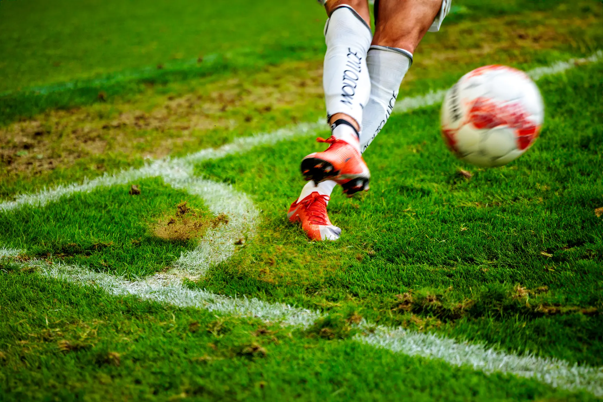 Ein Fussballspieler in weissen Stutzen und roten Fussballschuhen tritt auf einem Fussballplatz einen weiss-roten Ball
iso: 1600