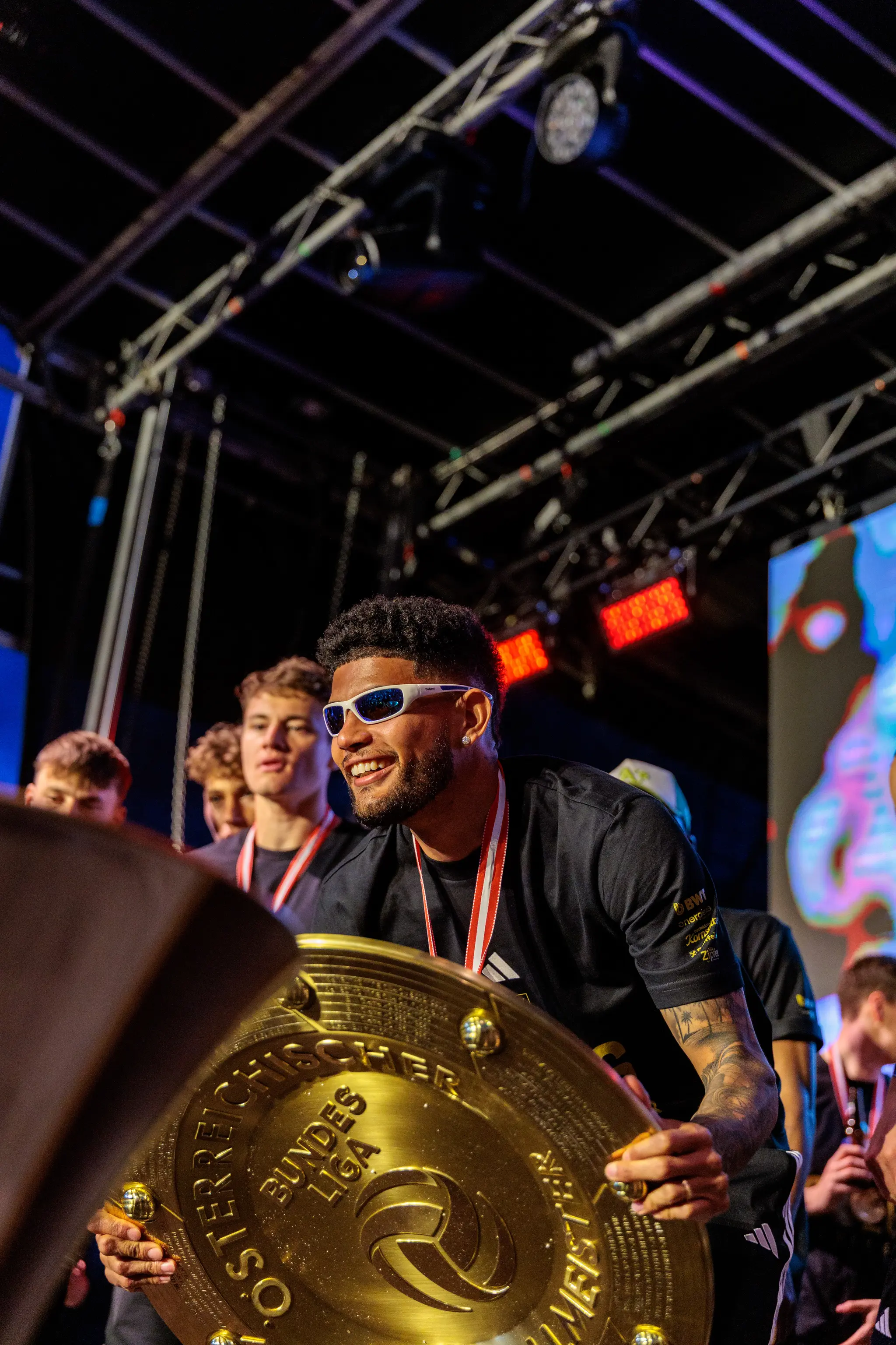 Ein LASK-Spieler mit weißer Sonnenbrille präsentiert stolz den goldenen Meisterteller während der Siegesfeier in Linz