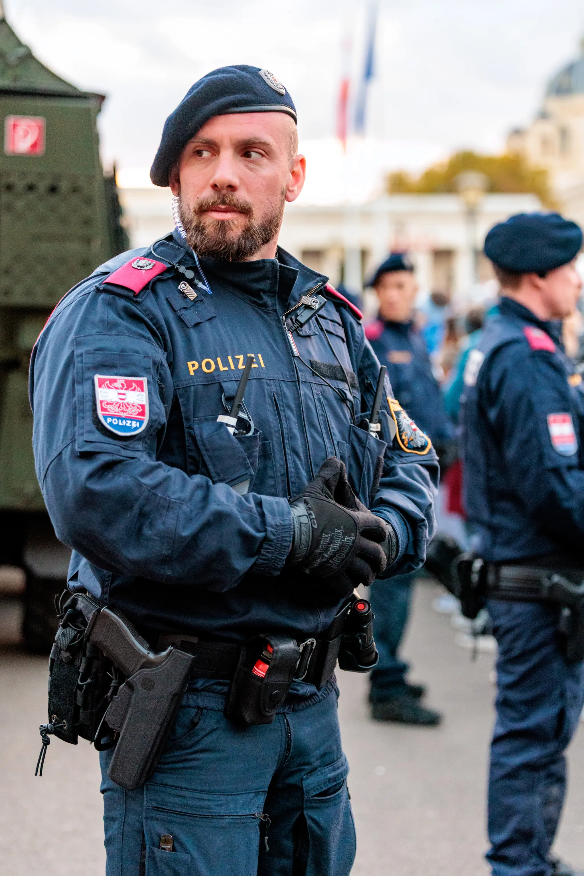Ein Polizist mit blauem Baret und dunkelblauer Einsatzjacke blickt am Heldenplatz nach vorn, die Hände vor dem Körper verschränkt.