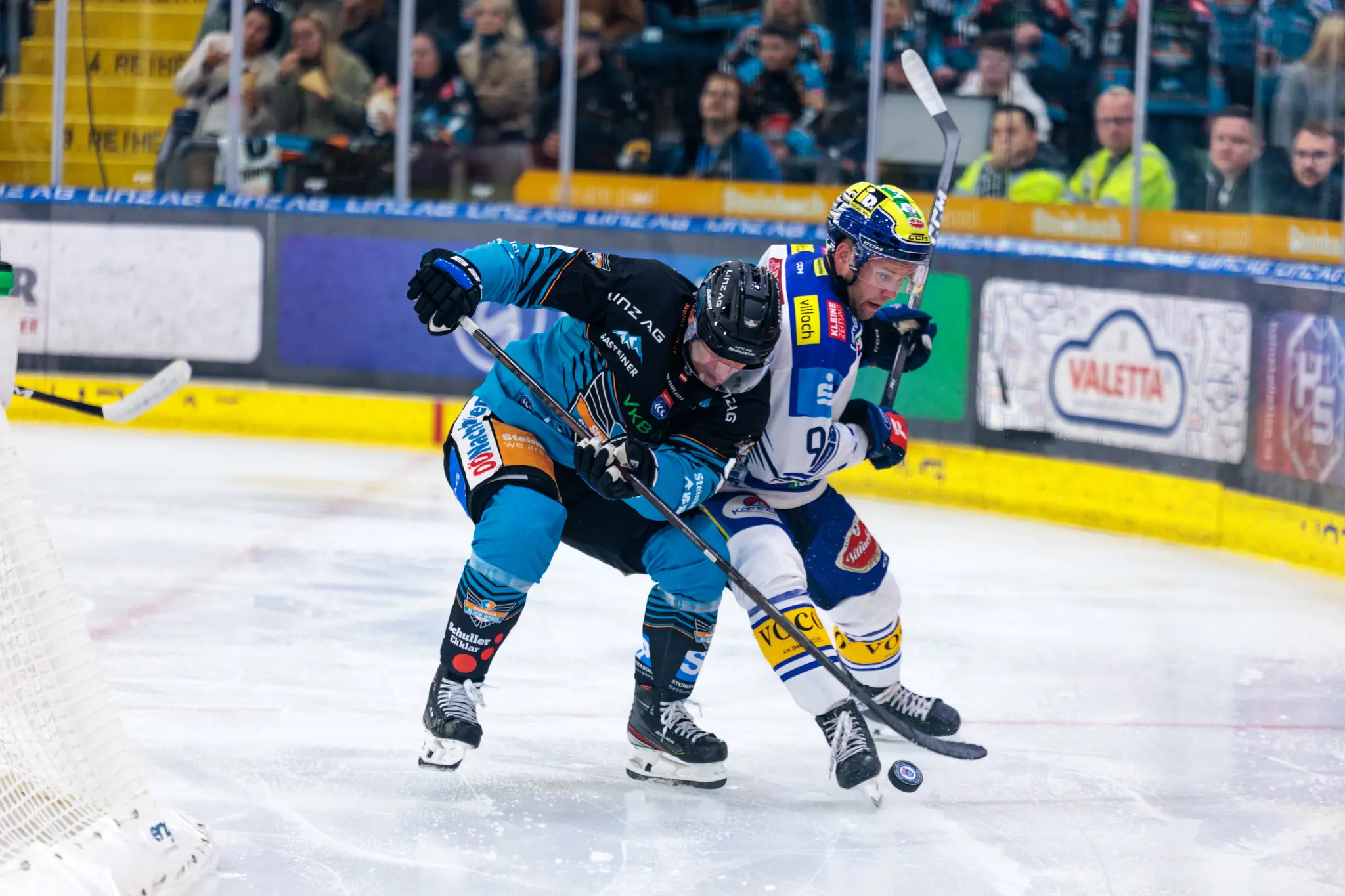 Aljaz Predan von den Black Wings Linz und Mark Katic vom EC VSV kämpfen während eines Eishockeyspiels intensiv um den Puck auf dem Eis