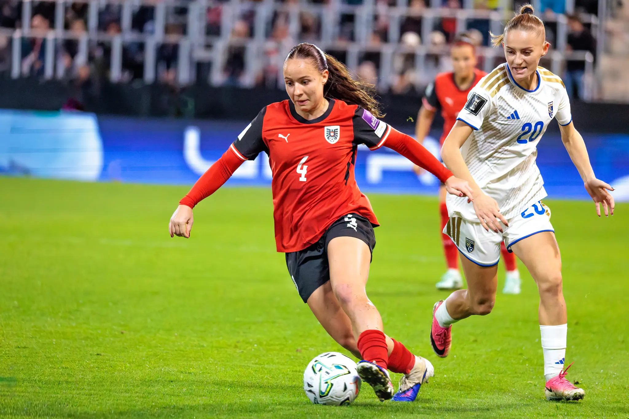 Valentina Pötzl (4) dribbelt mit dem Ball am Fuß, dicht gefolgt von Aurora Mulliqi (20) aus Kosovo.