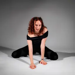 Clara Schmidhammer posiert ausdrucksstark mit ihren markanten roten Locken und einem schwarzen Off-Shoulder-Top für ein Porträt im Studio