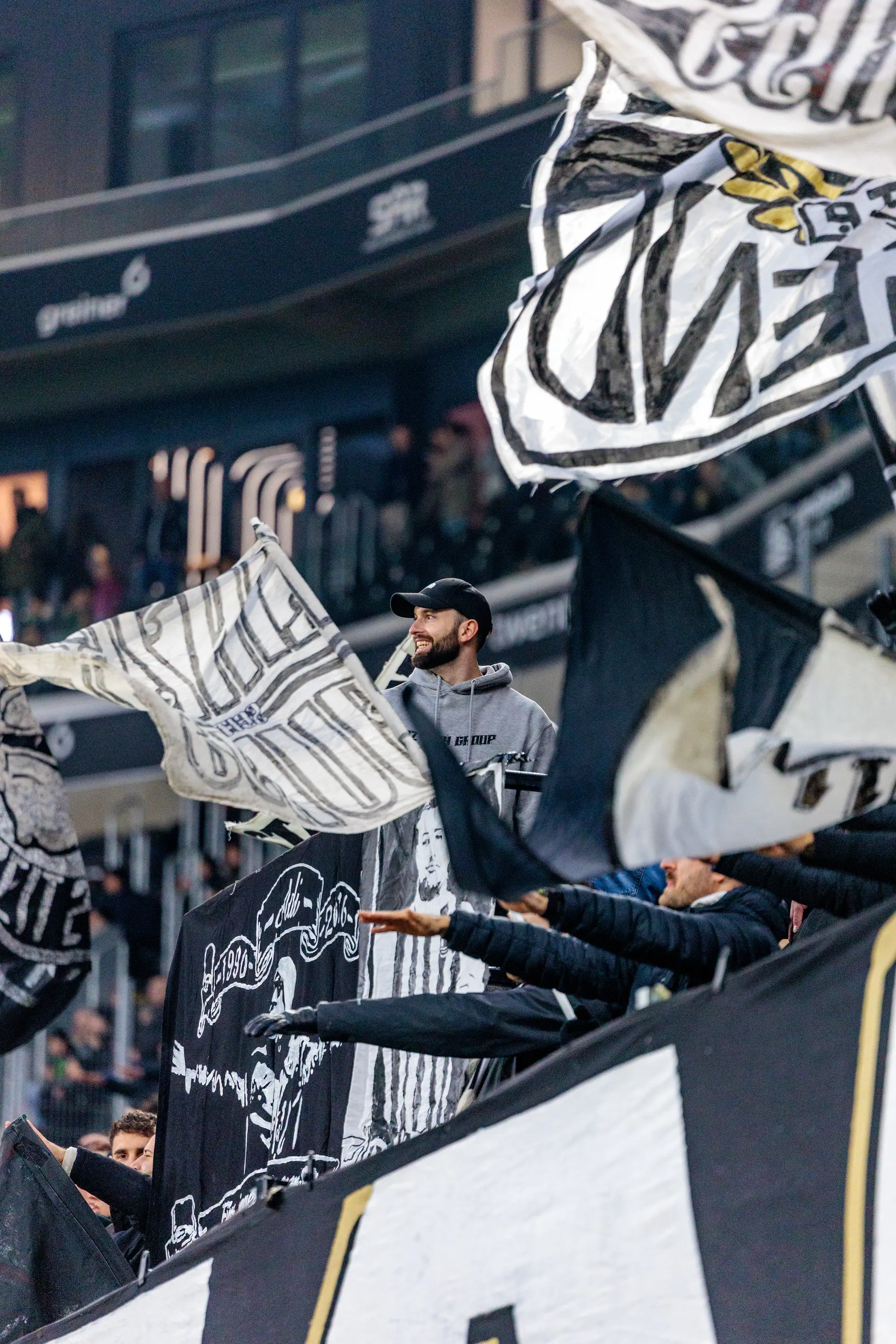 Begeisterte Fußballfans in der Raiffeisen Arena schwenken schwarz-weiße Fahnen während eines Bundesliga-Spiels