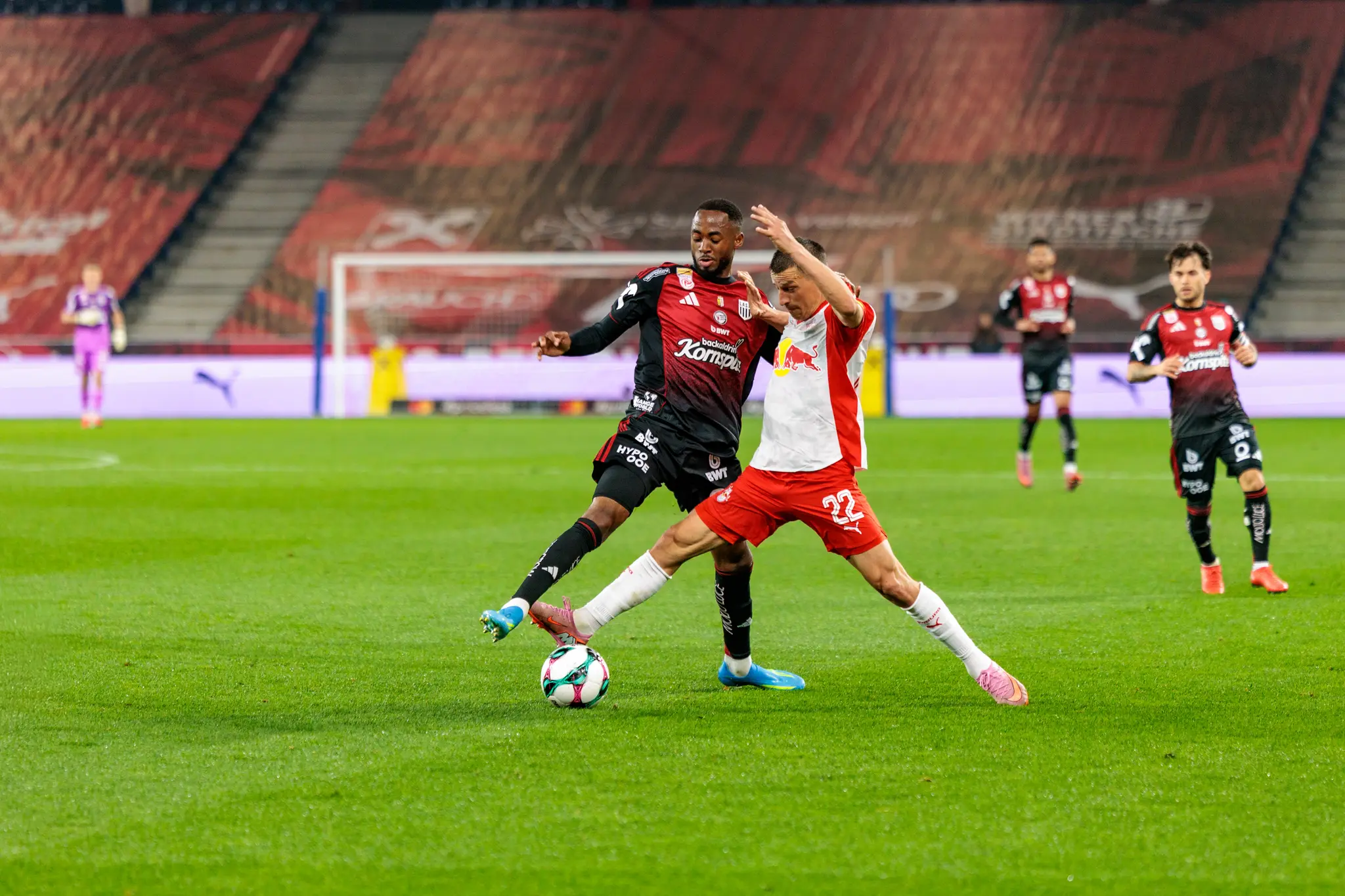 Zwei Fußballspieler, einer im schwarz-roten Trikot des LASK und einer im rot-weißen Trikot von Red Bull Salzburg mit der Nummer 22, duellieren sich energisch um den Ball