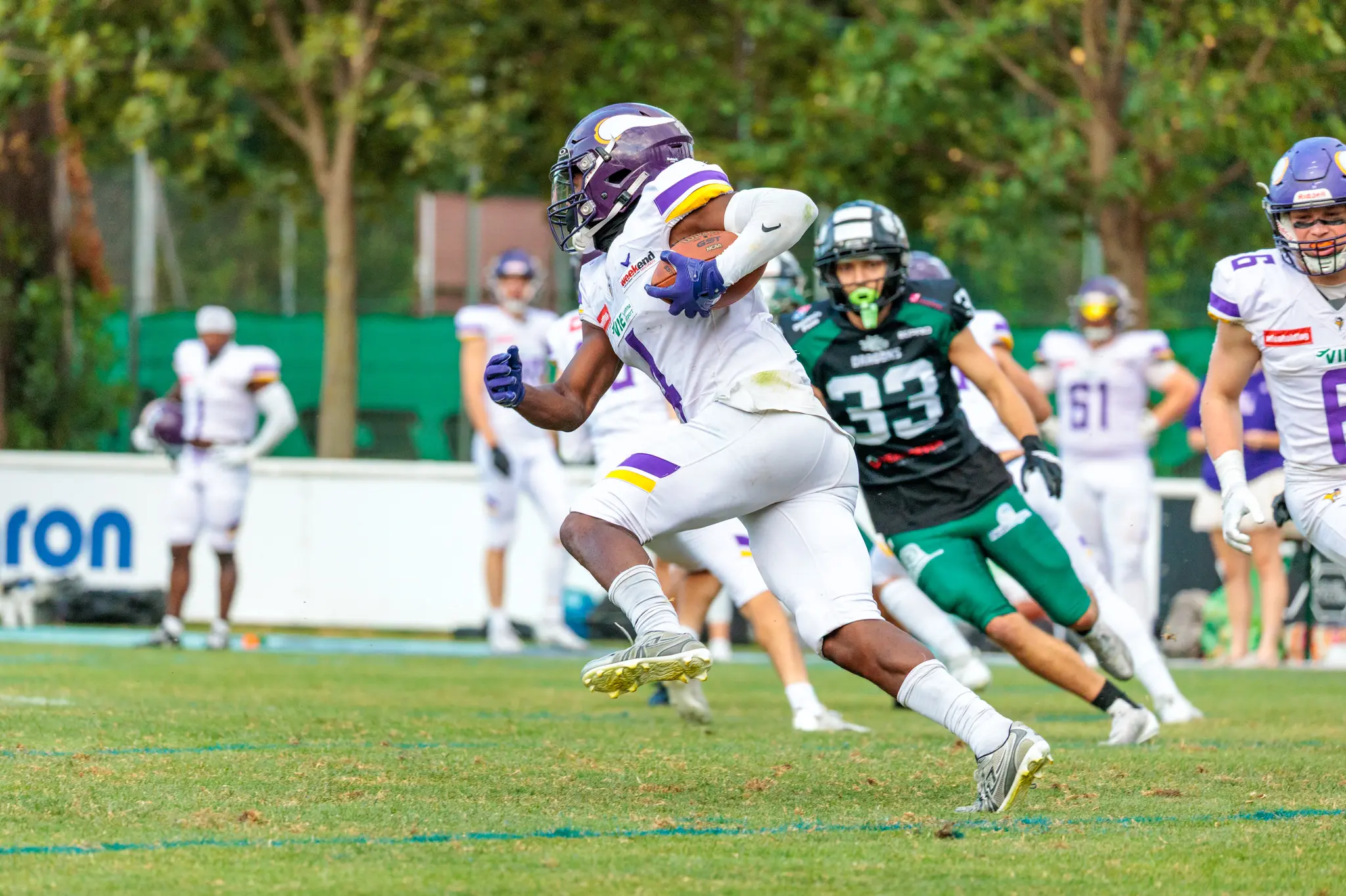 Vienna Vikings Läufer im weißen Trikot läuft den Ball an der Danube Dragons-Abwehr in grünen Trikots vorbei – AFL-Playoff 2026