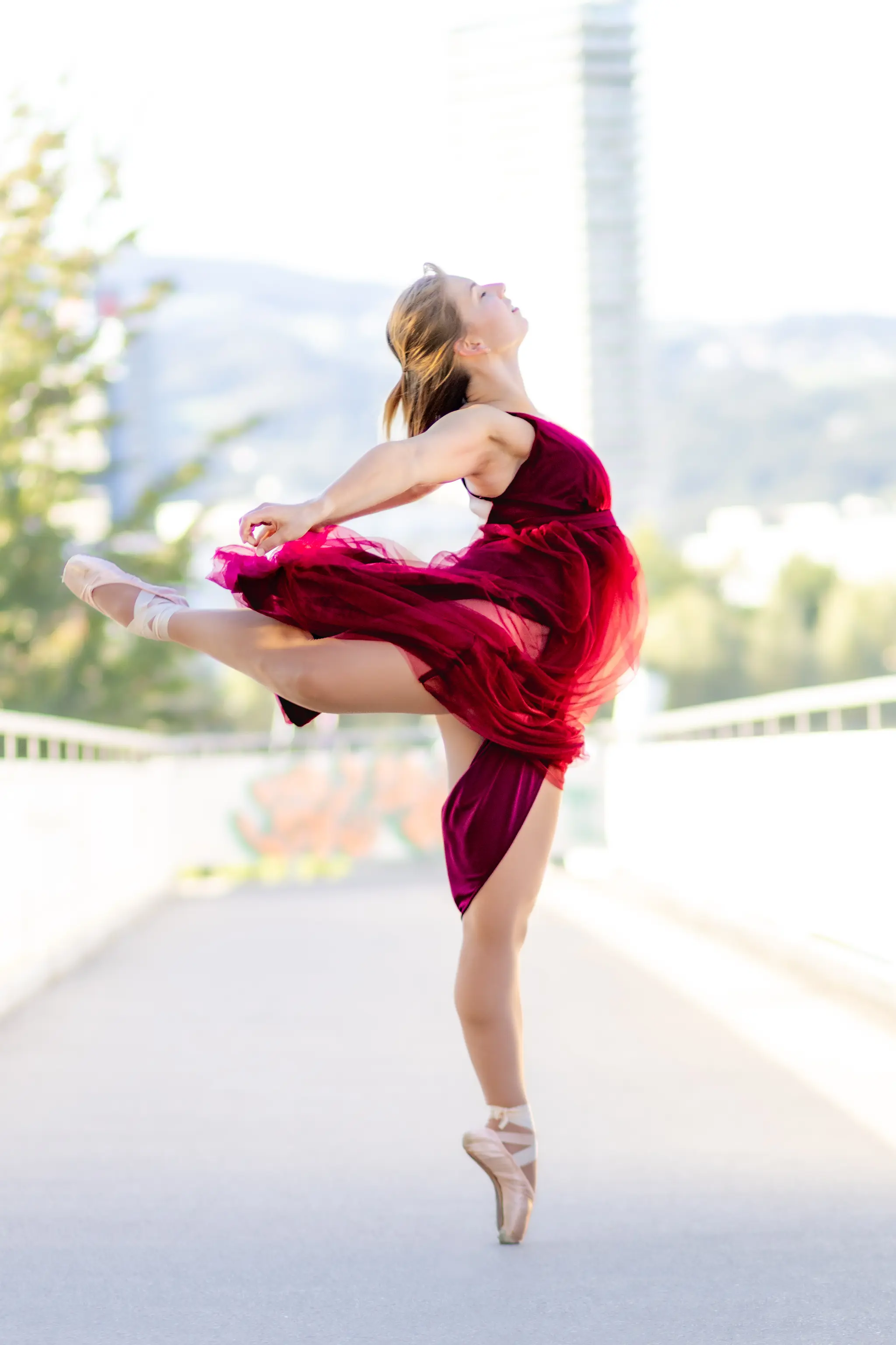 Eine Ballerina in einem weinroten Kleid tanzt elegant auf Spitzenschuhen auf einer hellen Promenade im Freien