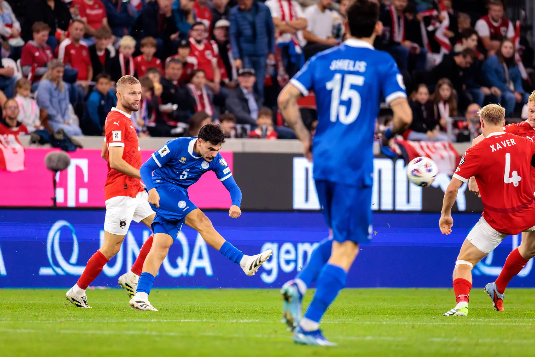 Der zypriotische Spieler Charalampos Charalampous (Nummer 5) schießt den Ball während eines WM-Qualifikationsspiels, während Xaver Schlager (Nummer 4) und Christoph Baumgartner (Nummer 19) von Österreich verteidigen
