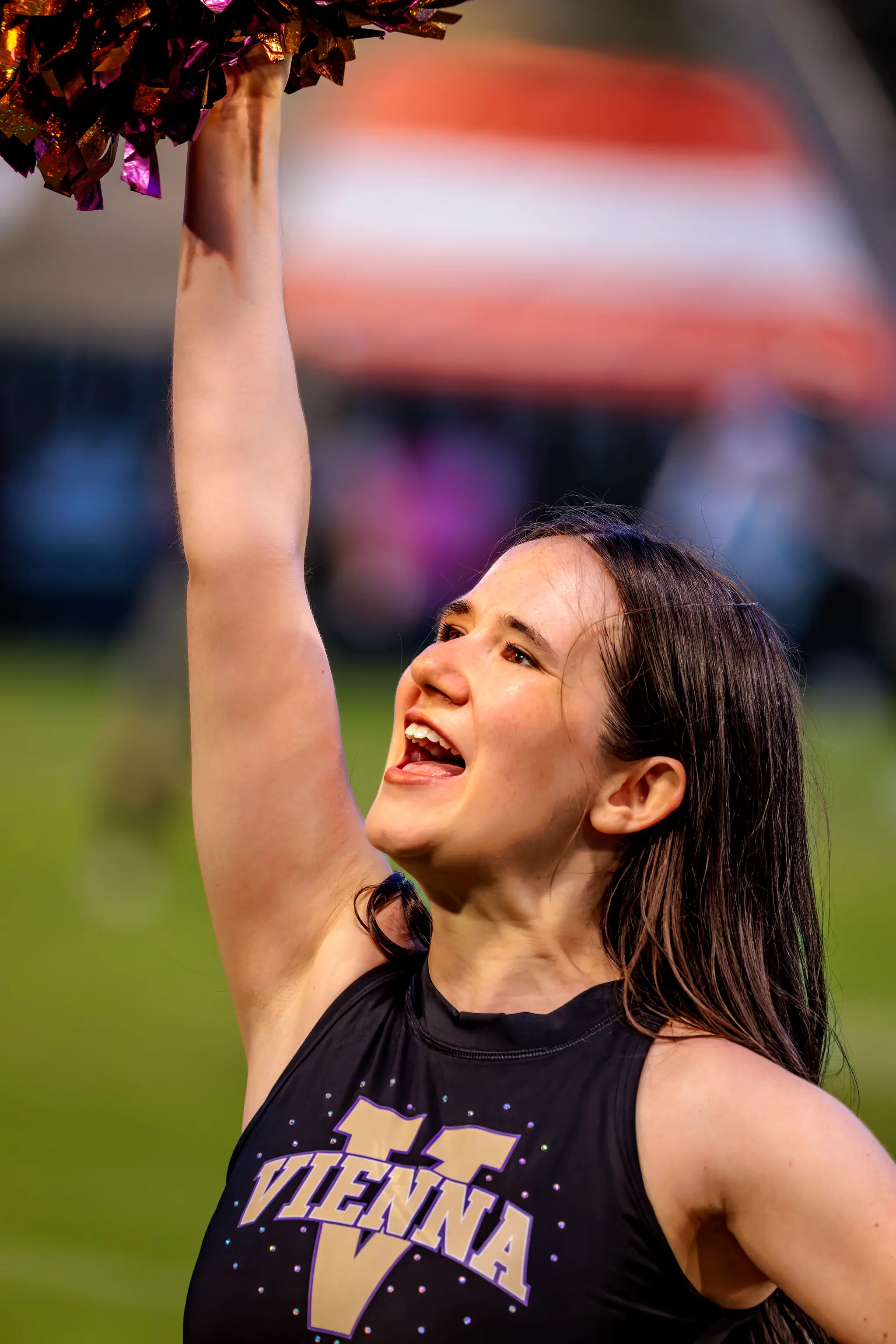 Cheerleaderin des Spirit Squad hebt einen violett-goldenen Pompon über den Kopf und lächelt.