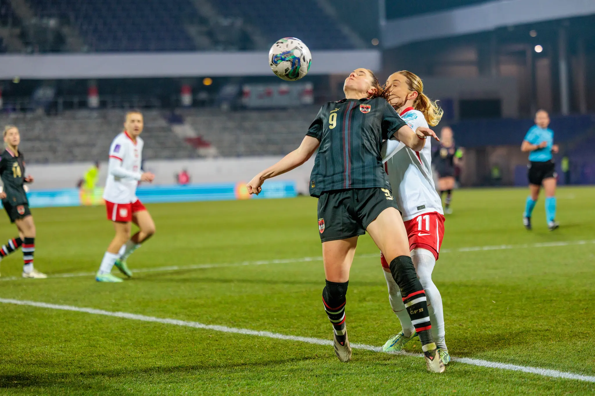Eine österreichische Fußballspielerin im dunklen Trikot köpft den Ball während sie von einer polnischen Gegnerin im weißen Trikot eng gedeckt wird