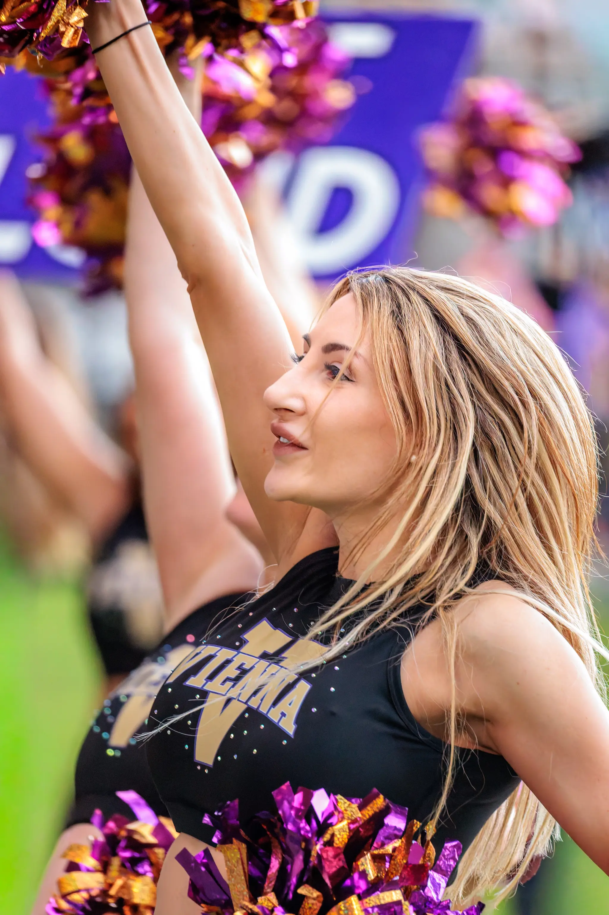 Profilaufnahme einer Tänzerin des Vienna Vikings Cheer Squads mit erhobenem Arm und lila-goldenen Pompons an der Hüfte.