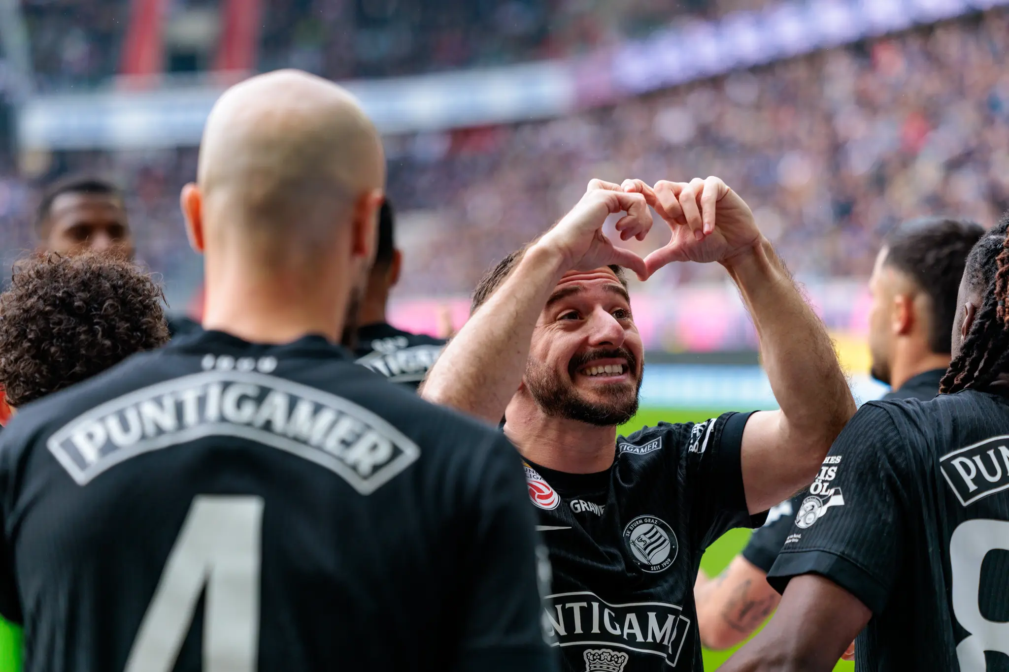 Ein lächelnder Spieler von Sturm Graz formt mit seinen Händen ein Herz als Torjubel vor den Zuschauern