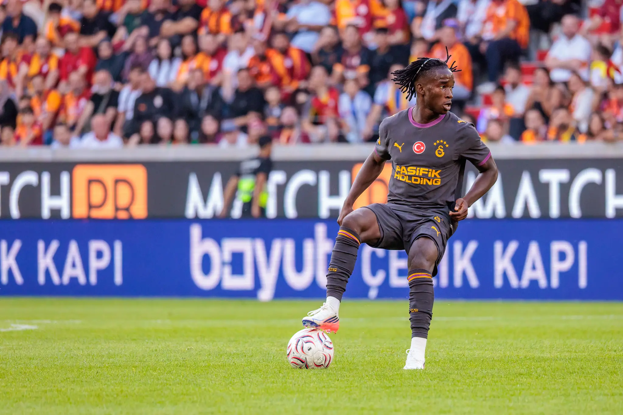 Galatasaray-Spieler mit Ballkontrolle am linken Fuß, Blick nach vorne, Publikum in den Tribünen im Hintergrund.