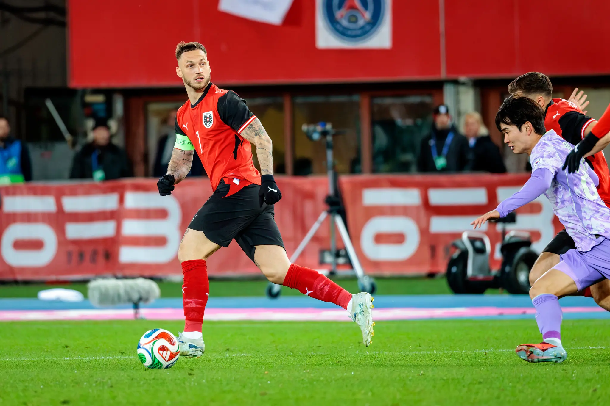 Der österreichische Fußballspieler Marko Arnautovic im roten Trikot sprintet mit dem Ball, dicht gefolgt von einem südkoreanischen Gegenspieler in lila