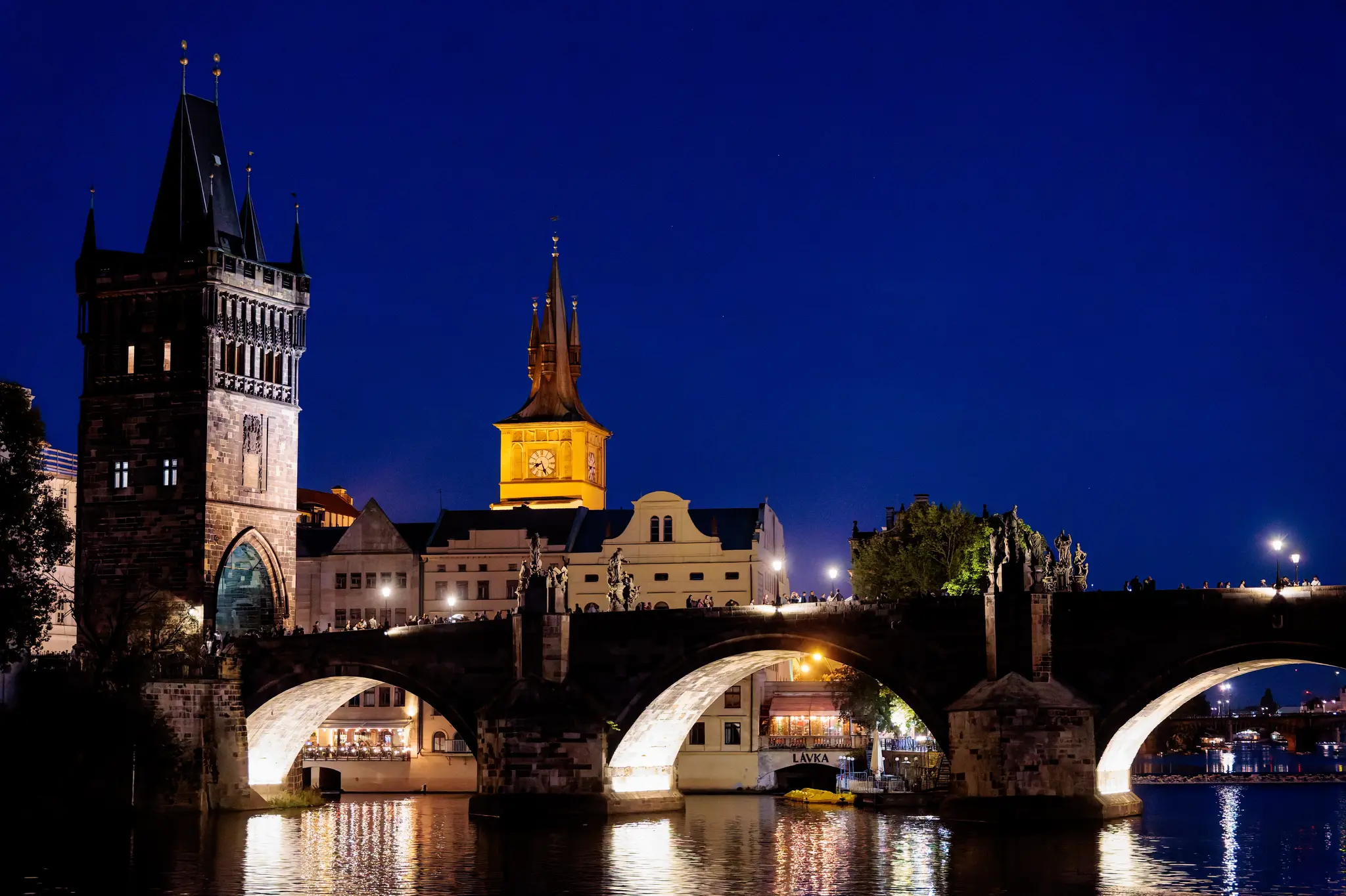 Der Altstädter Brückenturm und die Karlsbrücke leuchten im Abendlicht; dahinter erheben sich die Türme der Altstadt über dem Wasser.