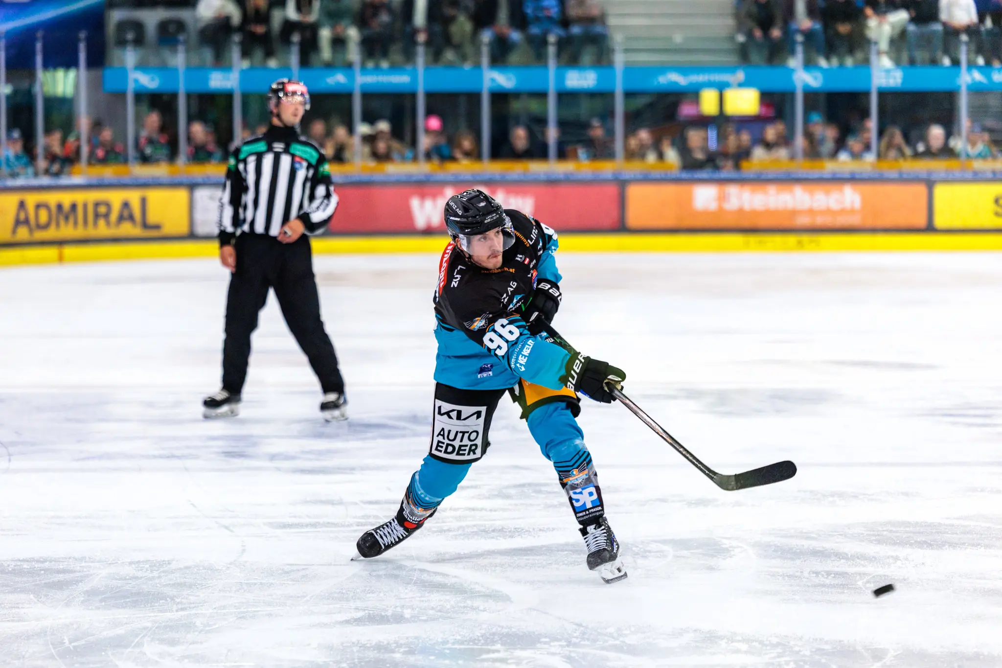 Eishockeyspieler Christoph Tialler in einem schwarz-türkisen Trikot mit der Nummer 96 schießt den Puck auf dem Eis während eines Spiels