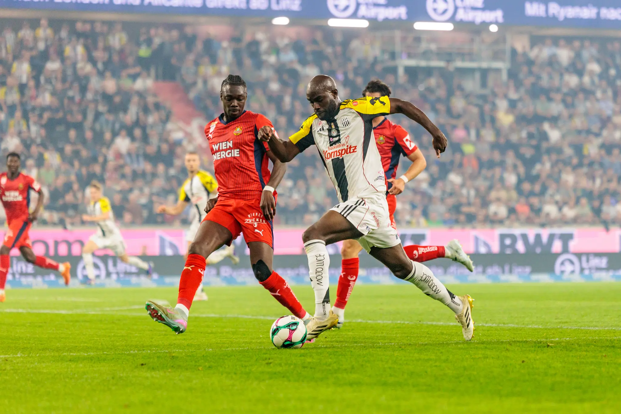 Ein Spieler des LASK behauptet den Ball im Zweikampf gegen einen Gegenspieler des SK Rapid während der Bundesliga-Partie